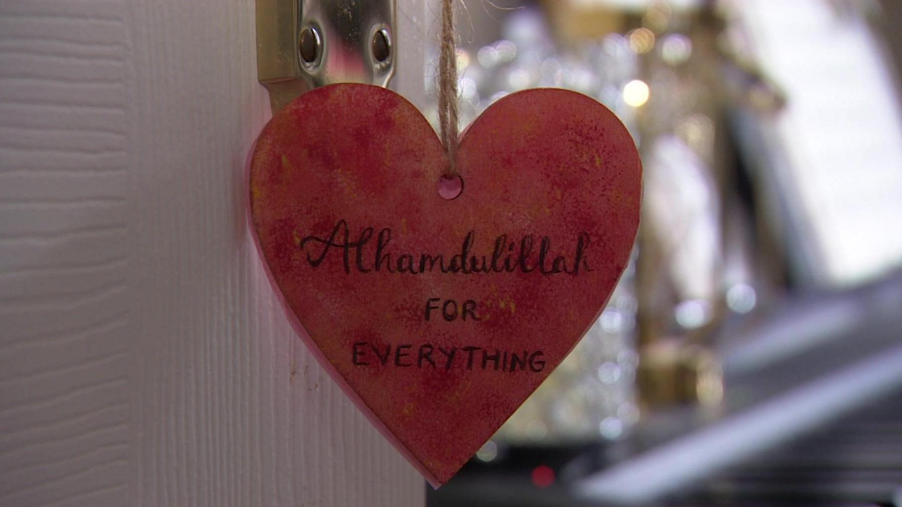 A wooden red heart hanging on a door handle. A slogan is written on the heart in black pen and reads: "Alhamdulillah for everything".