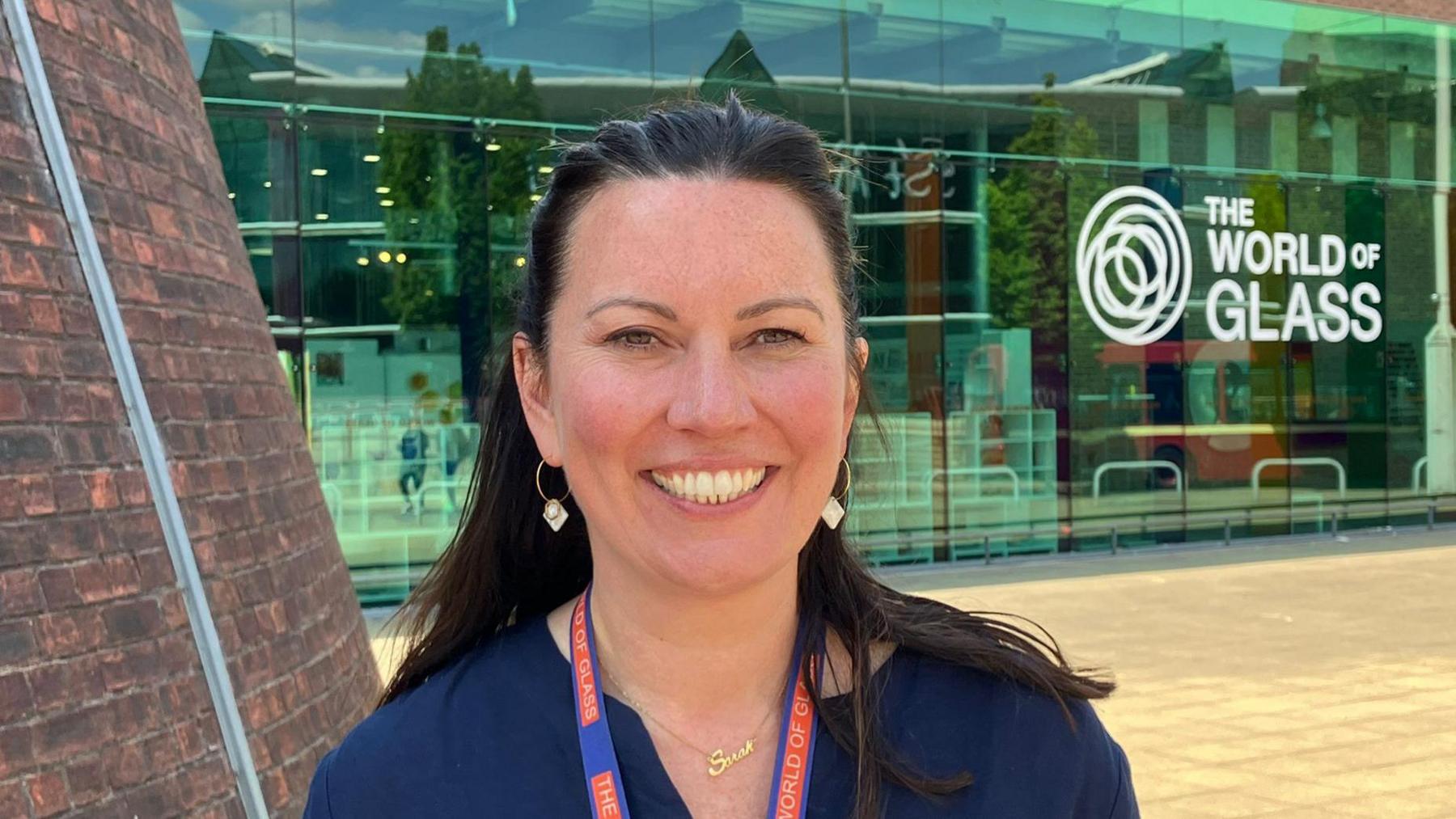 Portrait of Sarah Taylor smiling outside the museum's glass front, which has the World of Glass branding.