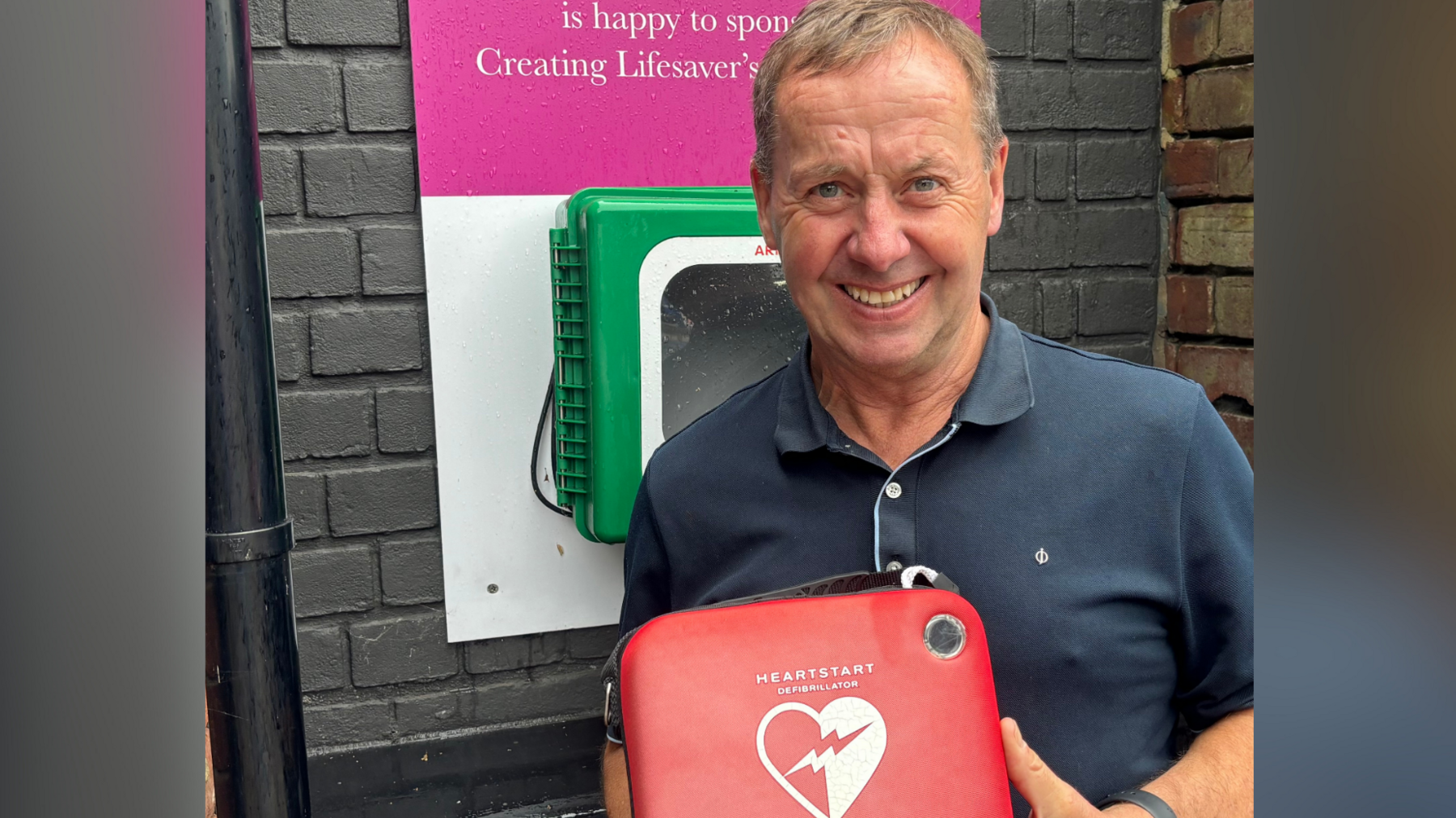 David Sullivan pictured outside a school where he installed a defibrillator. He is pictured holding the red AED machine.