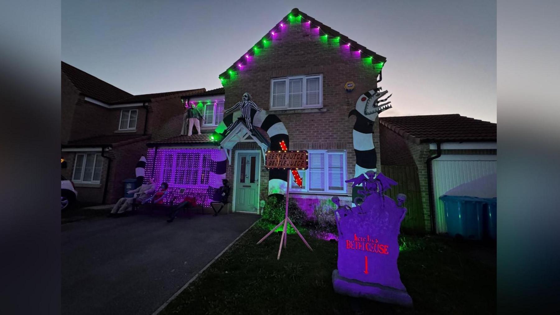 A suburban home has been decorated in the theme of the Beetlejuice film, complete with green and purple lights and large black and white decorations.