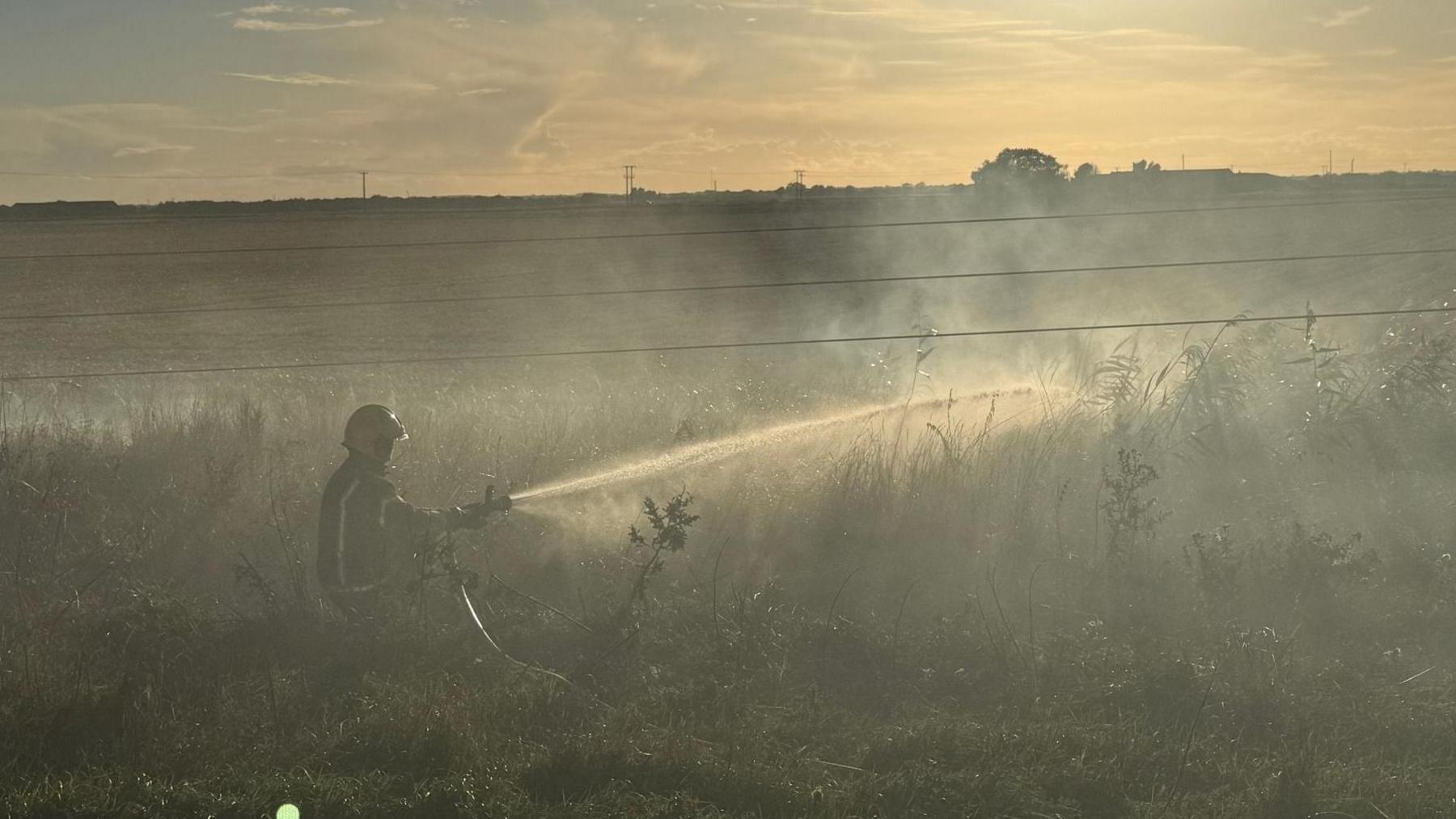 Firefighter at sunset - water coming from a hose. Electric wires are running across the image.