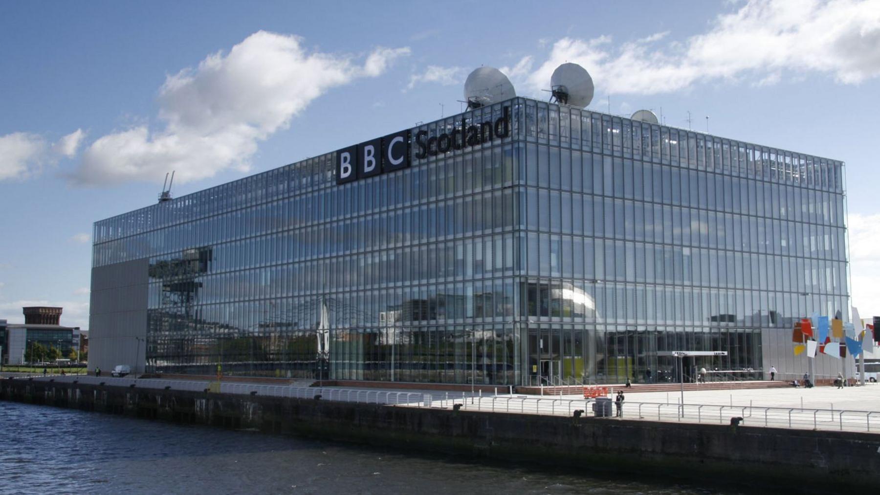 A large glass box building with windows on all sides and satellite dishes on top