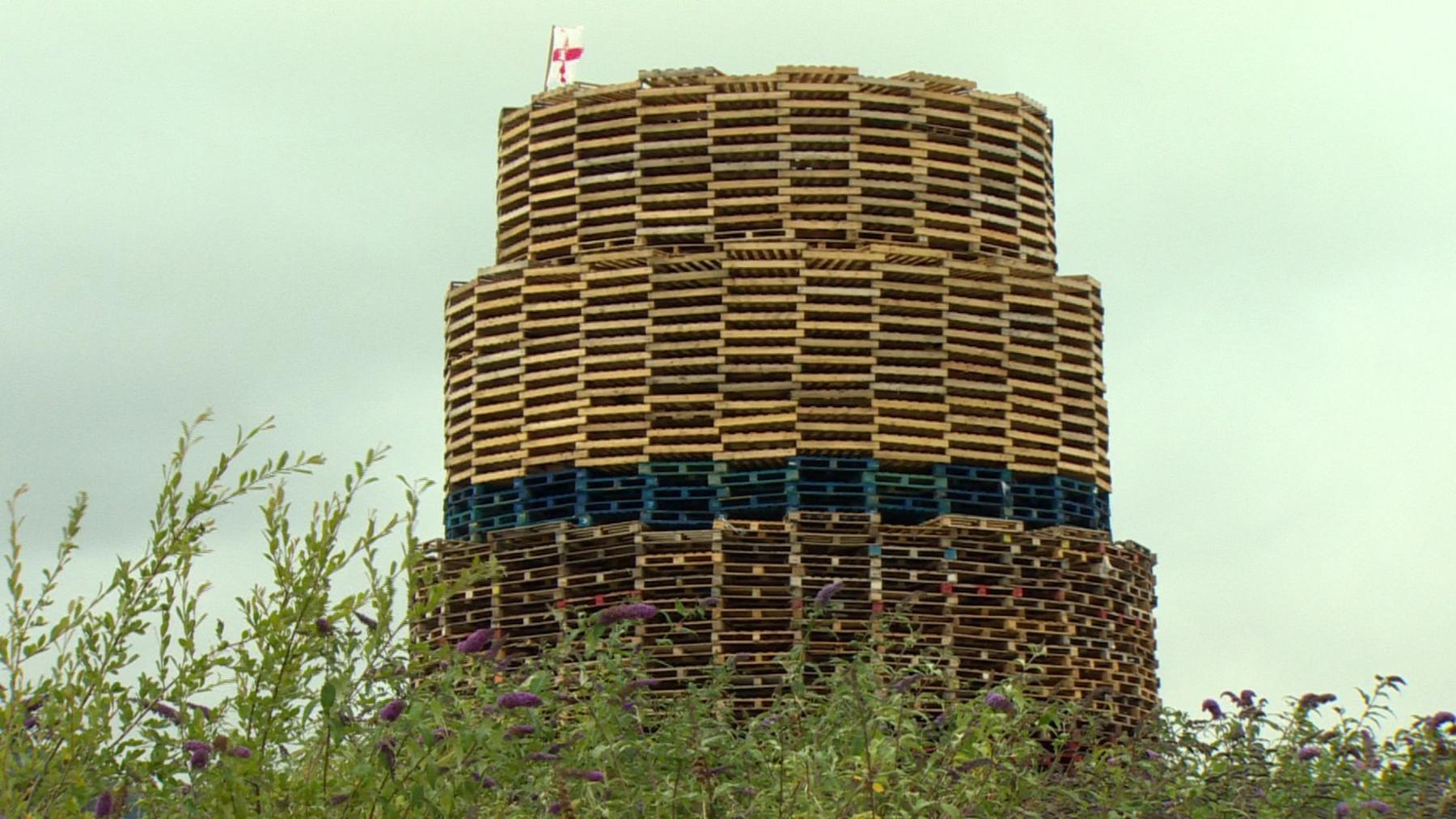 The bonfire that's built with red, white and blue pallets. Below is some shrubbery.