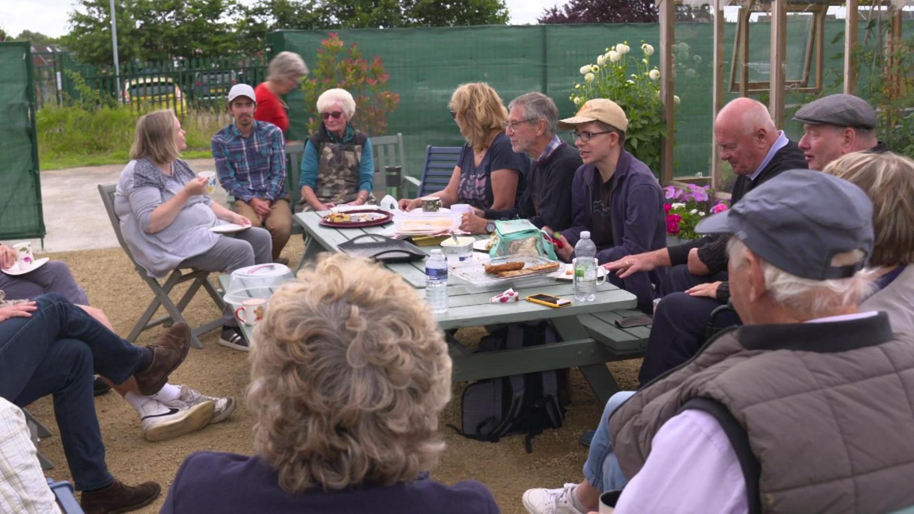 Volunteers sit around a large picnic table eating cakes