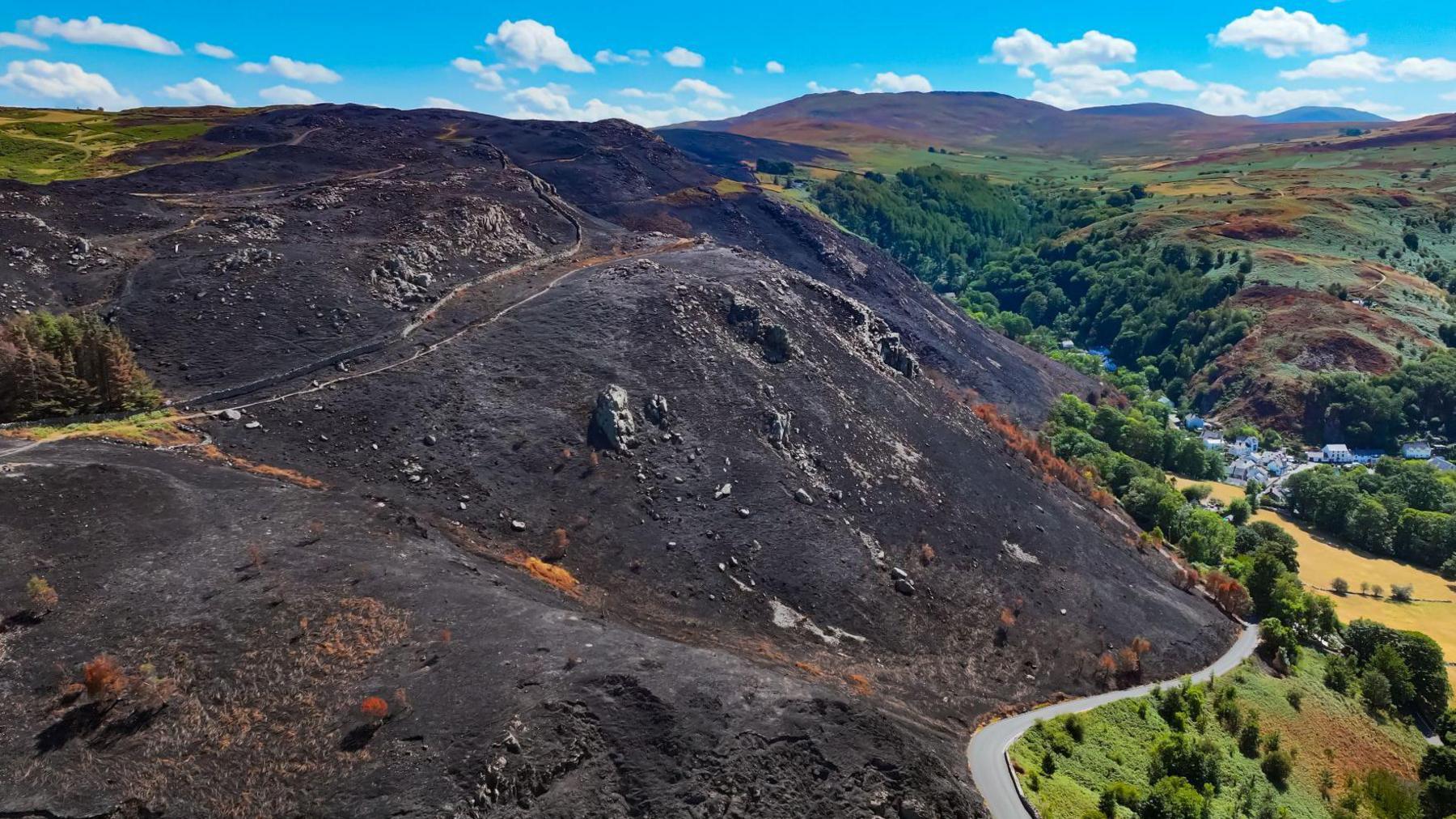 An aerial picture of the Sychnant Pass, which looks completely black. It shows how close the fire came to houses at the foot of the mountain.