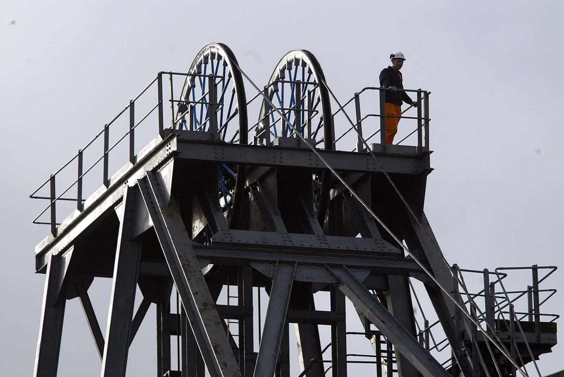 Ellington colliery in Northumberland. A man in a hi-vis and hard hat stands on top of a grey steel structure containing two lift wheels at the pit head.