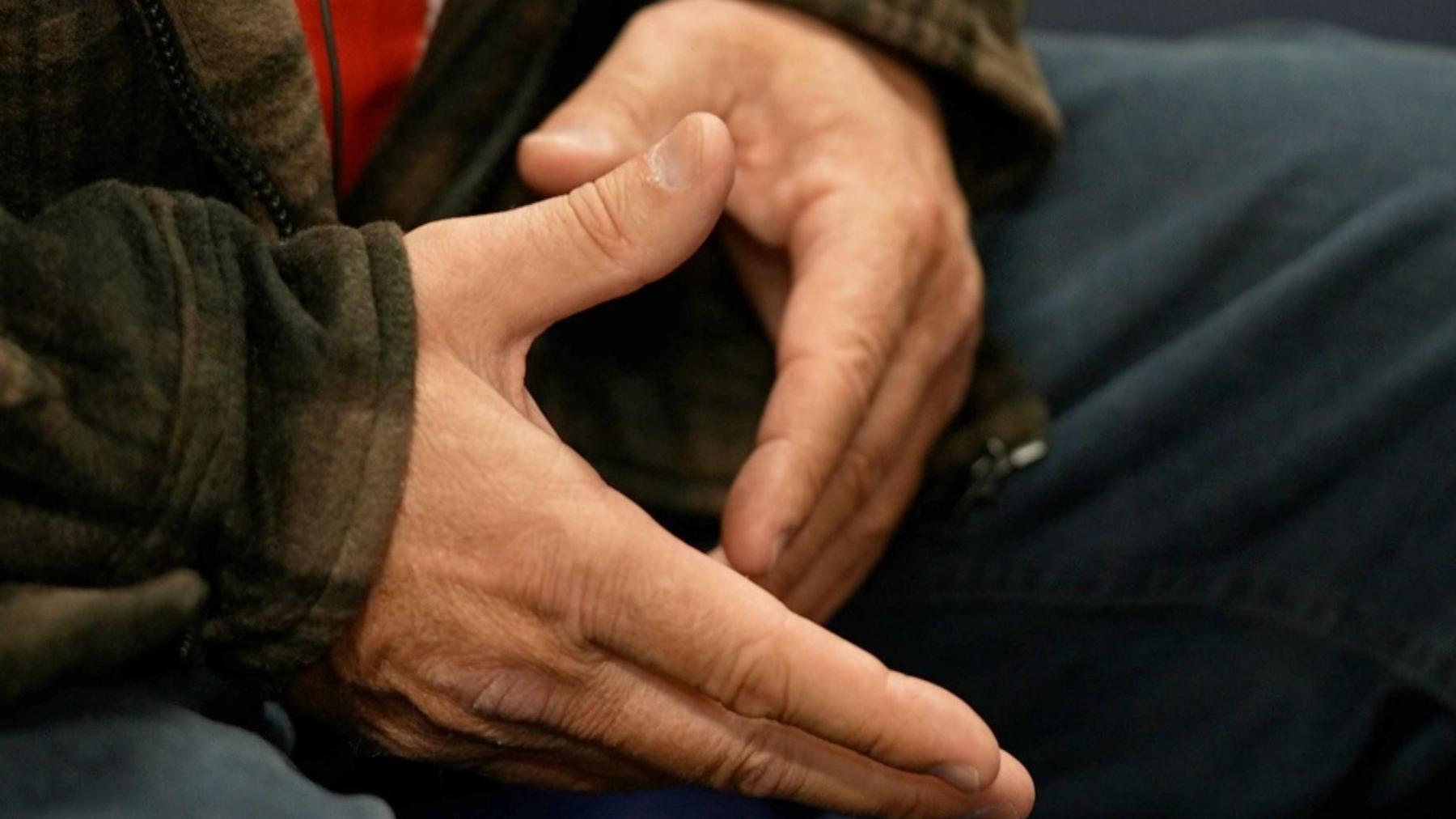 A close up image of a pair of hands, the person is also wearing dark blue jeans and a green jacket. 