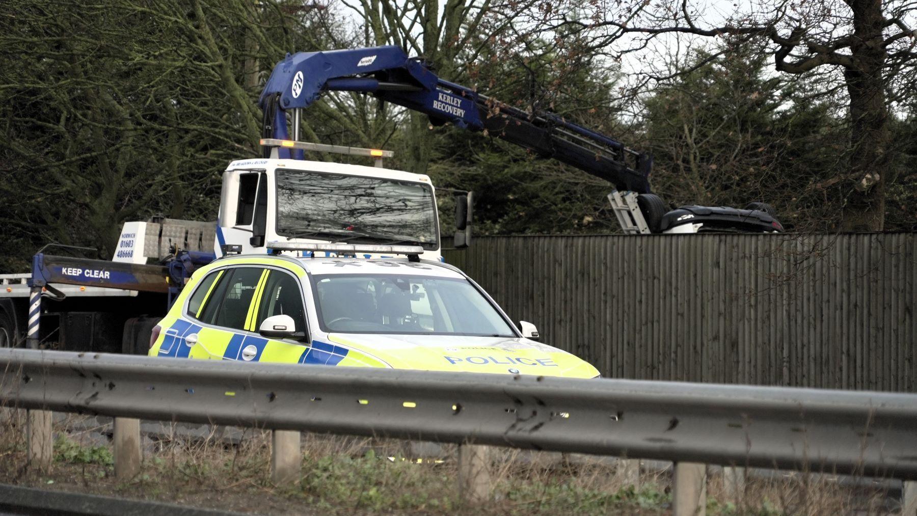 A police car on a road. Behind it is a white and blue recovery vehicle