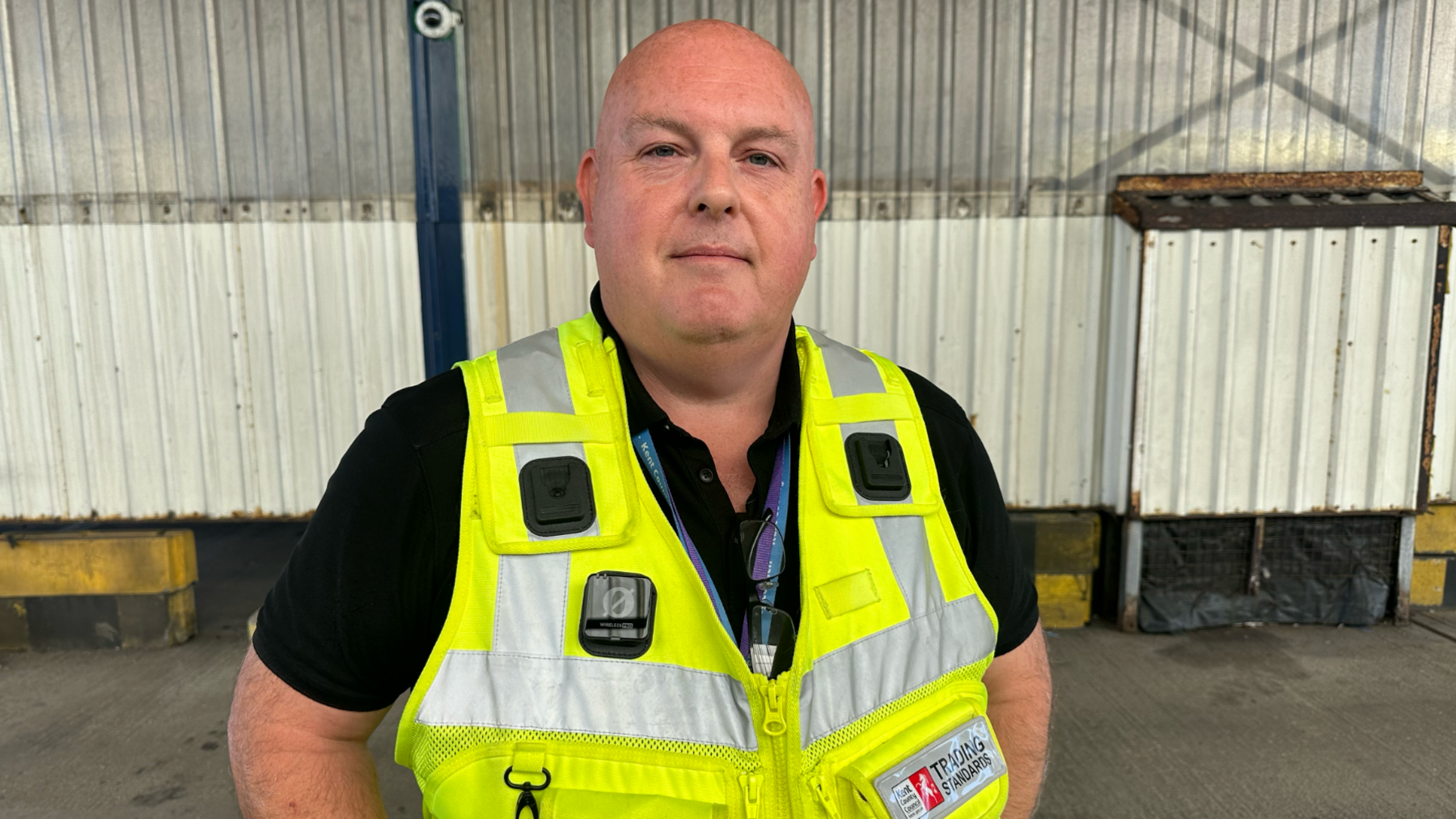 Trading Standards officer Jason Chappell standing in a freight lane at the Port of Dover wearing a high visibility jacket smiling at the camera