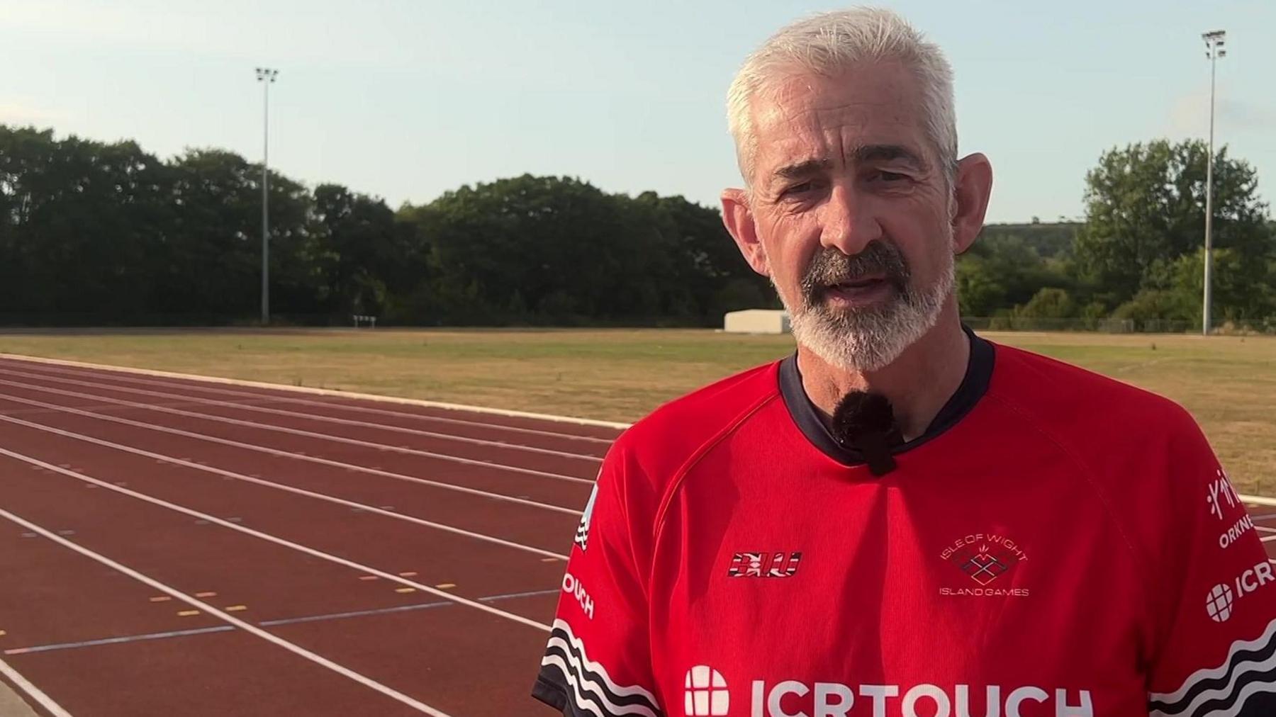 Kevin Winchcombe in a red Isle of Wight top, standing on an athletics running track