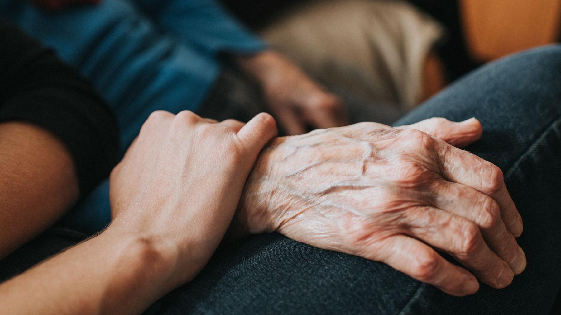 An elderly person's hand being held by a younger person