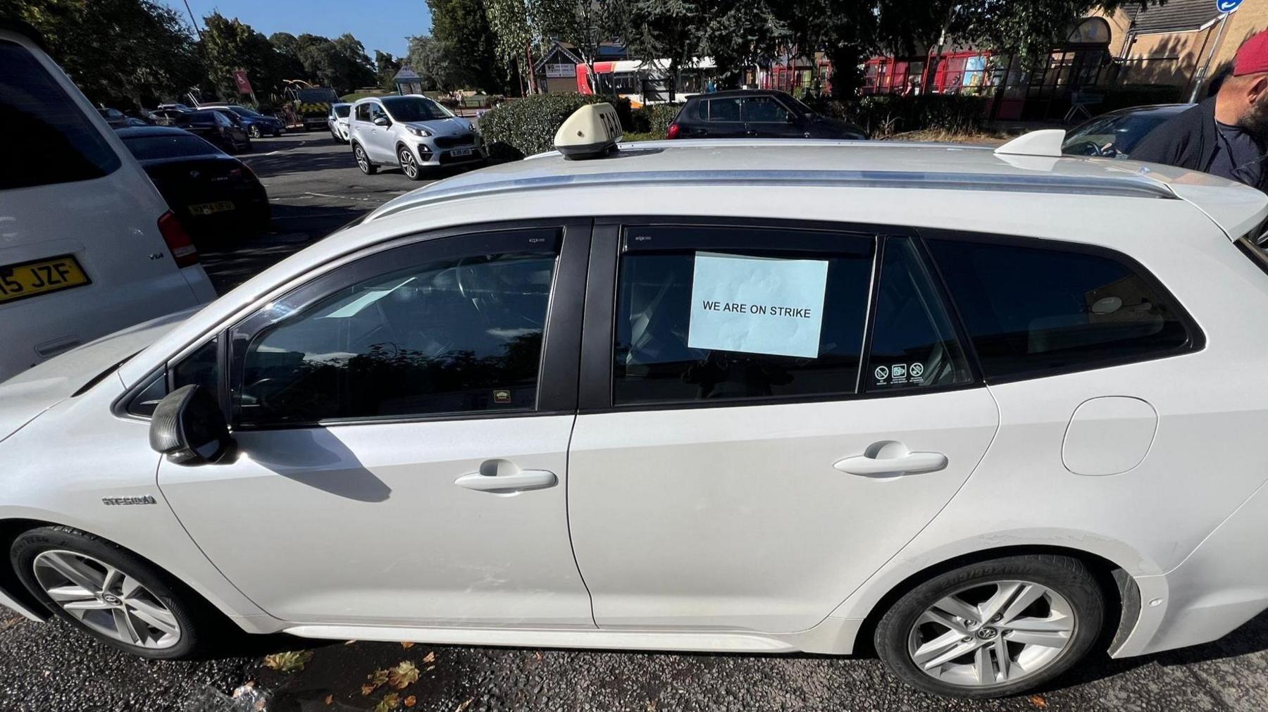 A parked silver car with a blue paper sign that says "we are on strike" in the window.