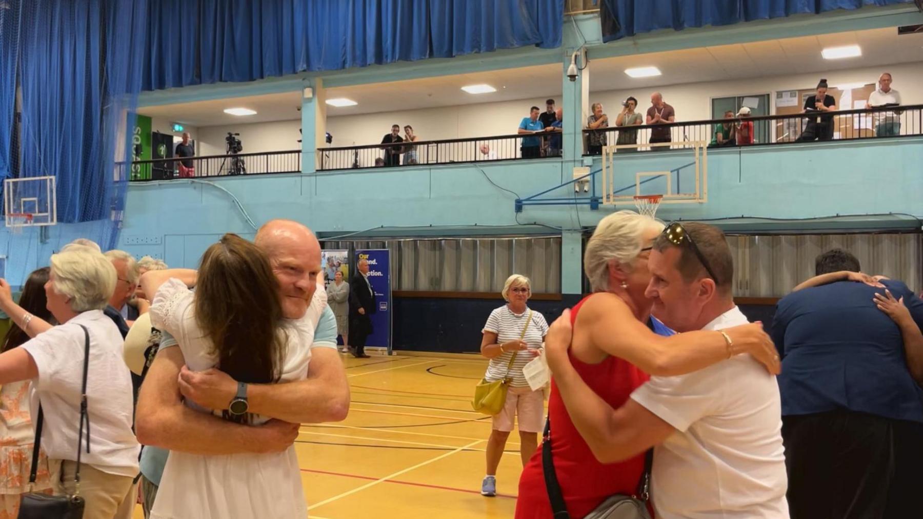 Two men hug women in a sports hall.