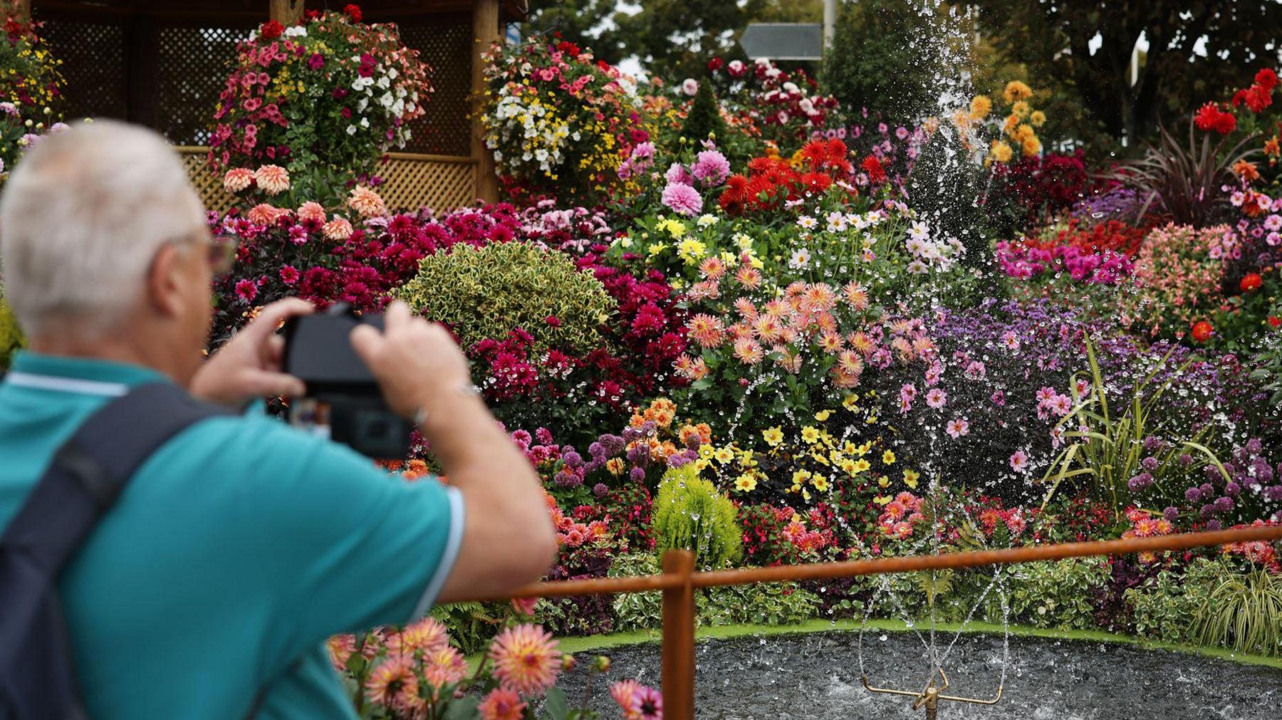 A man wearing a blue t-shirt taking photographs of a large floral display