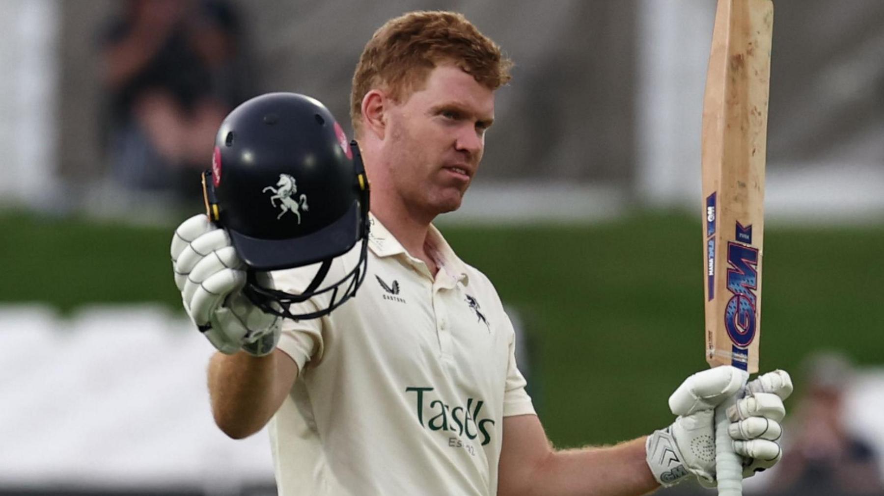 Kent's Ben Compton raises his bat in his left hand and blue Kent helmet in his right to acknowledge the crowd after scoring a century against Leicestershire at the Spitfire Ground on 30 July 2025