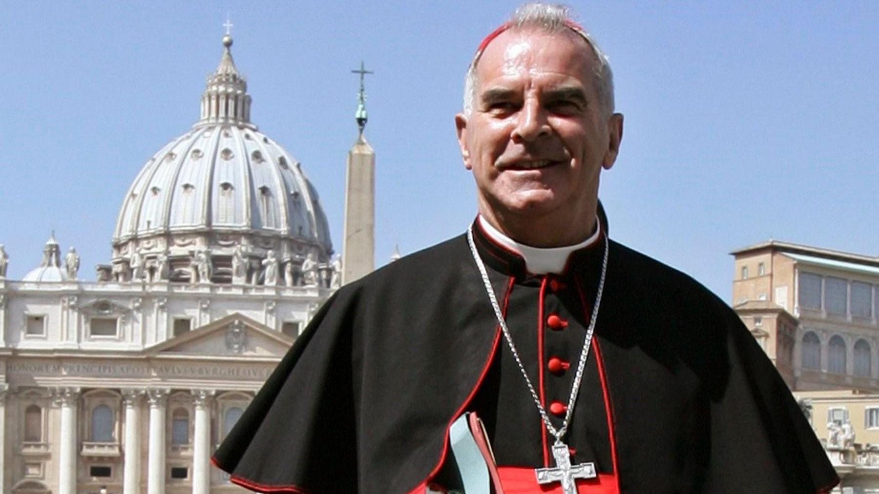 Cardinal Keith O'Brien wearing cassock and with silver crucifix standing in St Peter's Square in Rome with St Peter's dome in the background