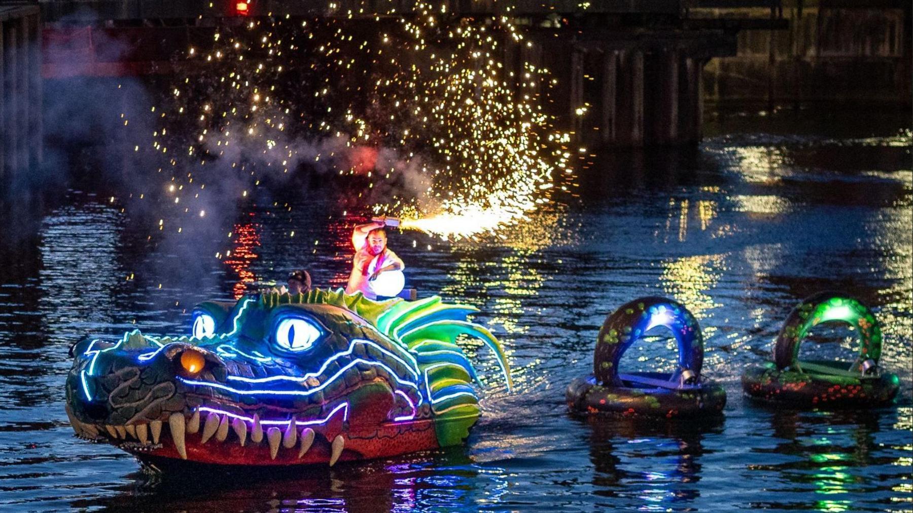 A man is waving a flare while riding the Monty the Mersey Monster display on a dock