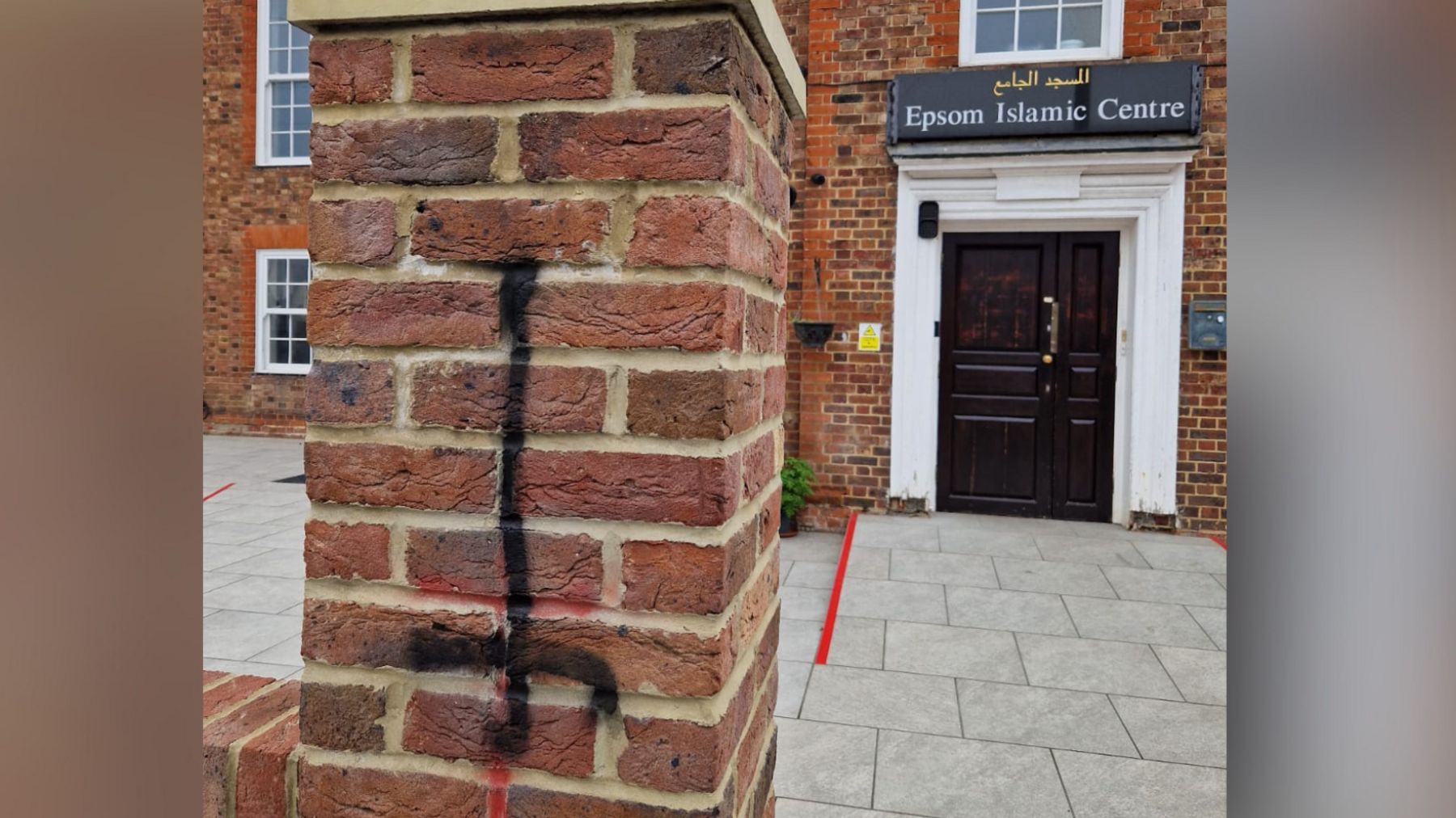 A graffiti of an inverted cross sprayed on a brick fence. Behind the fence is a mosque.