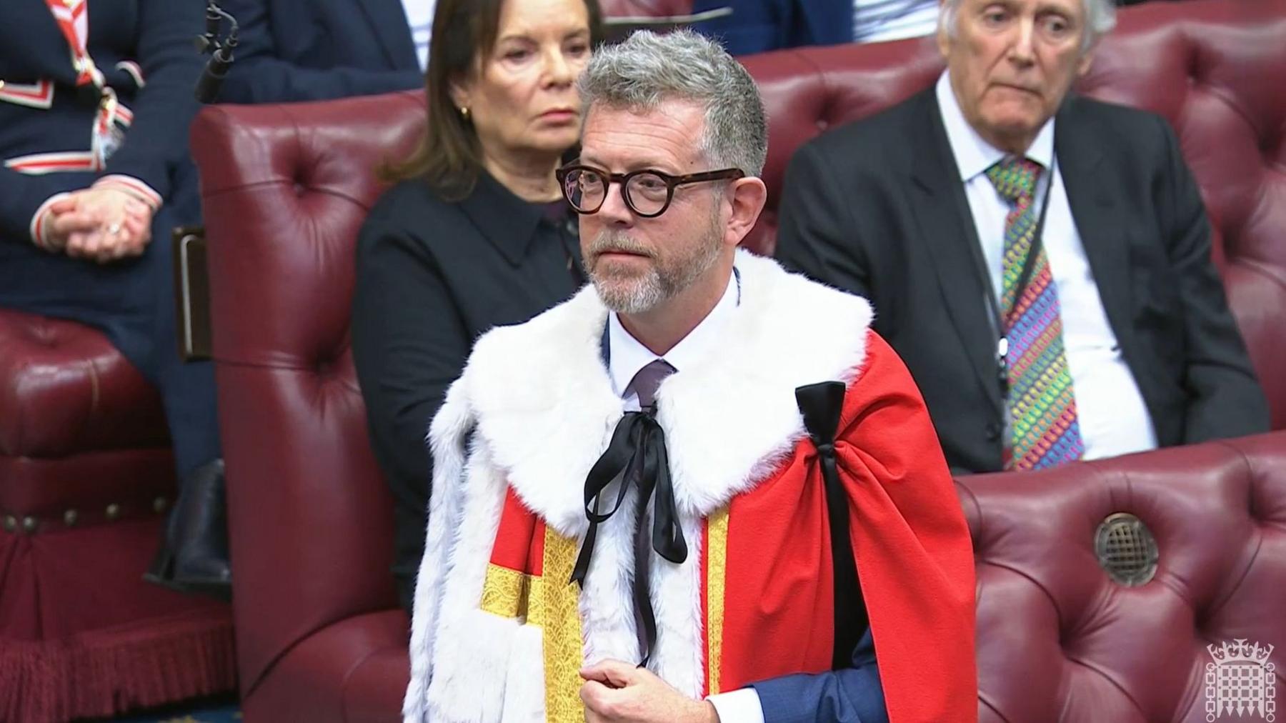 Lord Doyle stands in the House of Lords in formal robes with peers sitting behind him.