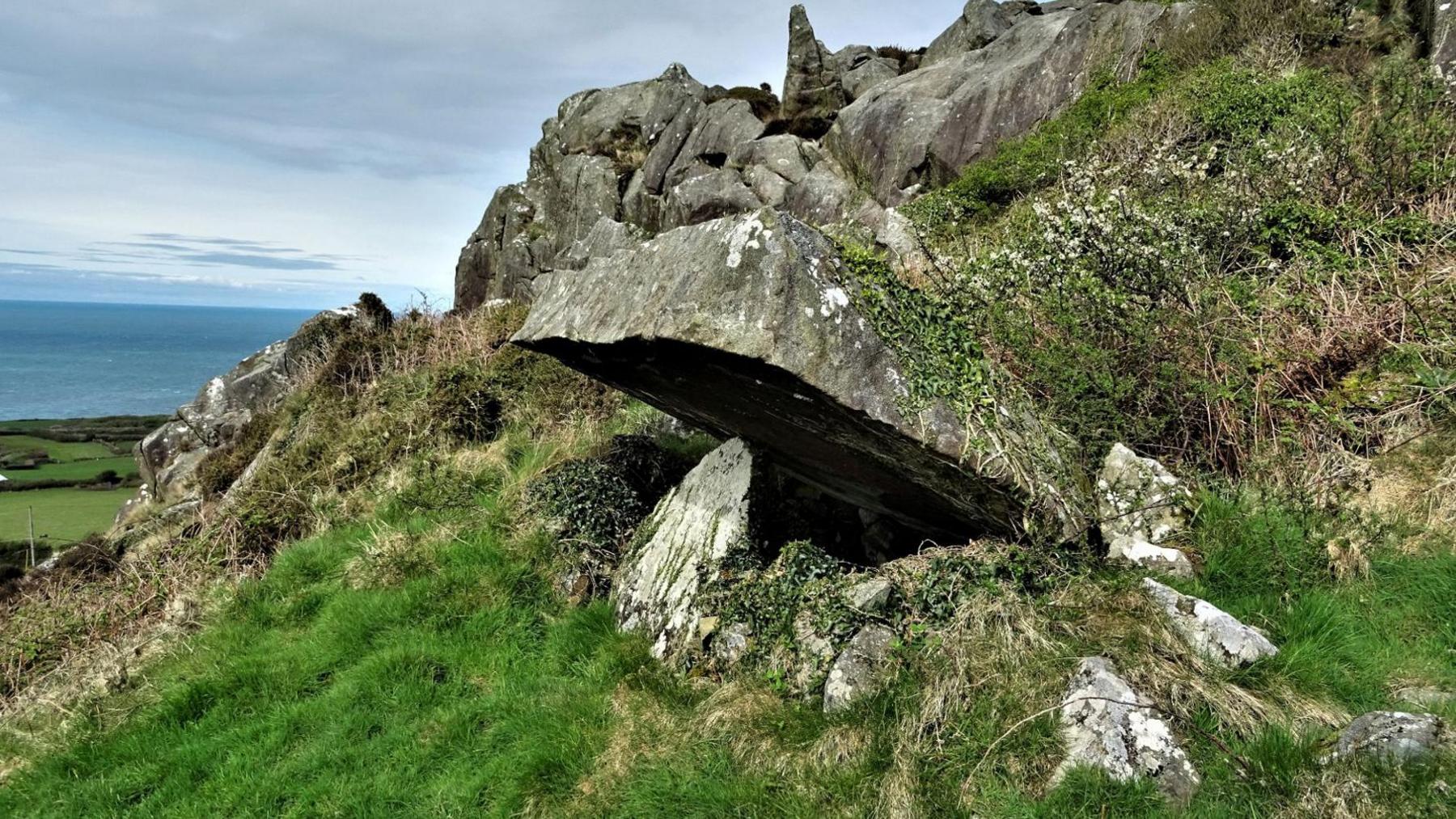 A flat capstone supported be a single upright overlooking the sea.