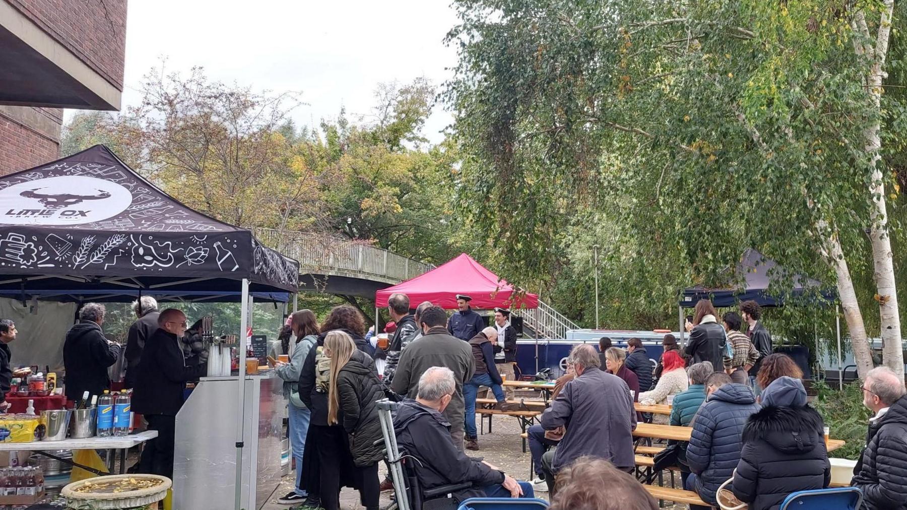 A crowd of people at Mount Place during Jericho's Oktoberfest on 17 October. Some are buying food and drinks while others are watching a band perform. A tent branded Little Ox Brew can be seen. It is cloudy.