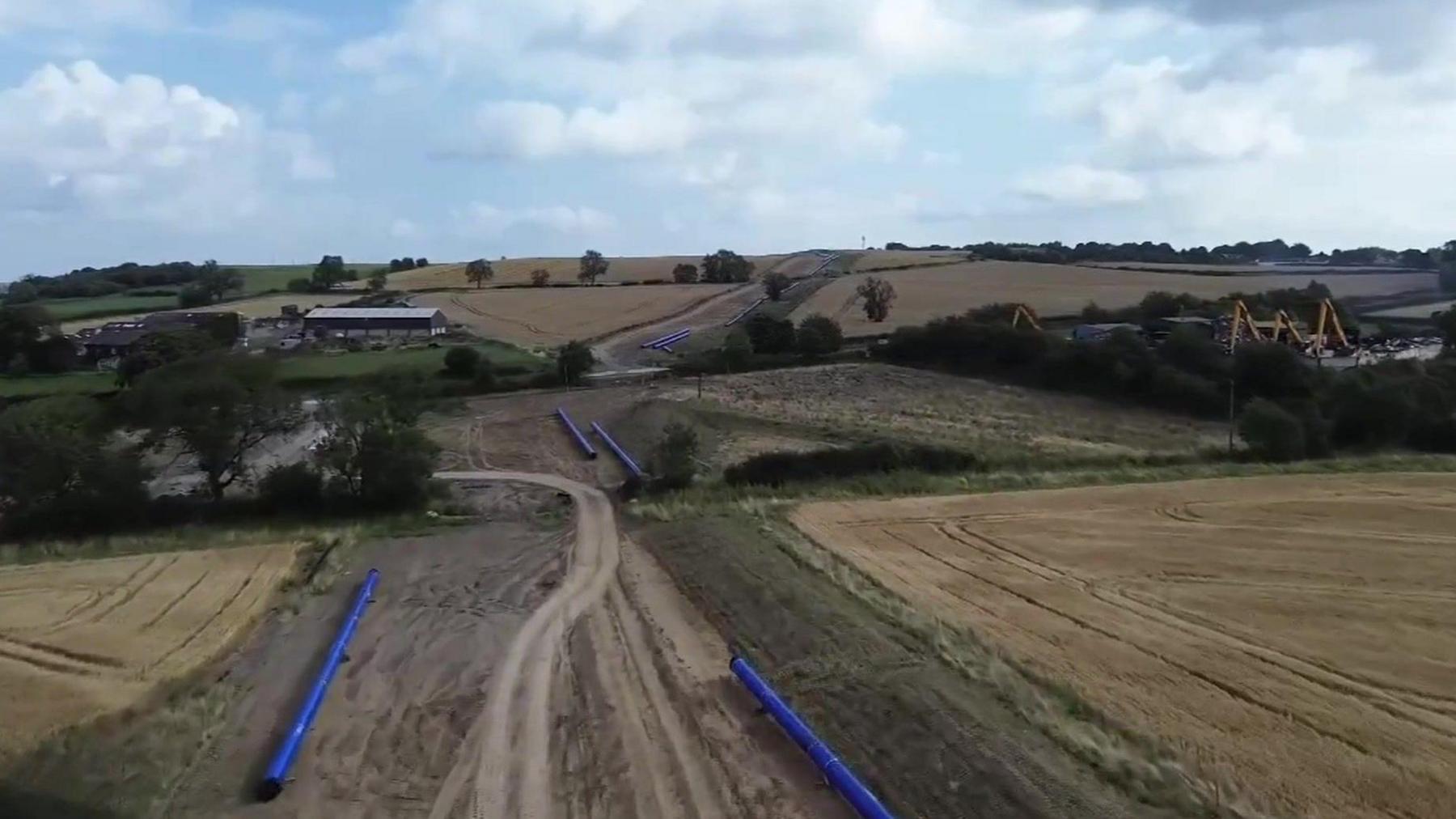 A landscape of fields with blue pipes lying alongside a dug-up area running through the middle.