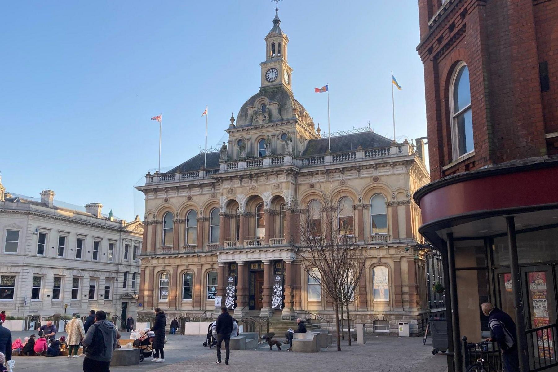 Ipswich Town Hall - the exterior of the ornate sandstone building with two high ceilinged stories and a dome and clock on the top. It overlooks a public square.