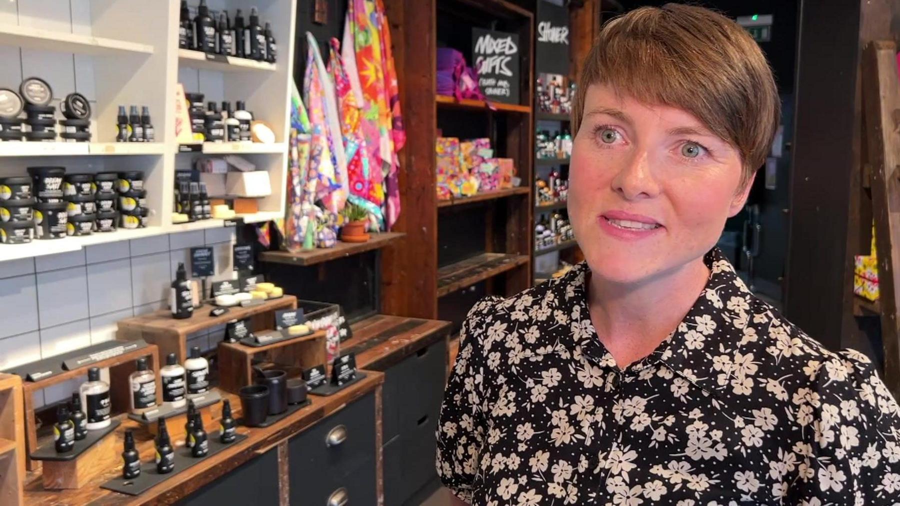 Kasey Swithenbank wearing a floral shirt is pictured in the Hull Lush store in front of an array of shampoos and soaps and multicoloured washcloths