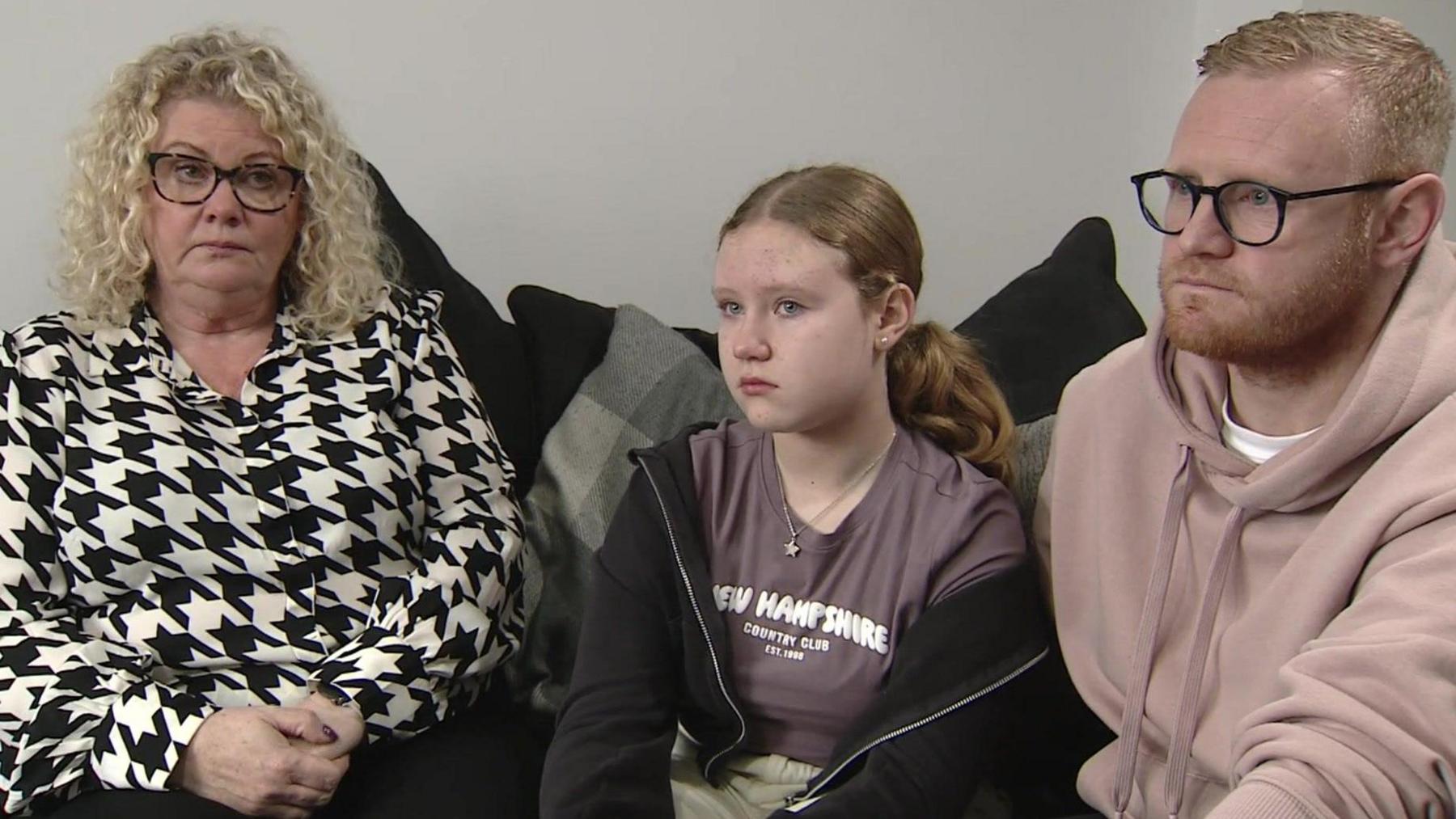 Helen, Connie and Lee sitting together on a sofa - Helen is wearing a black and white checked pattern blouse, Connie wearing a black zipped top and lee wearing a light brown hoodie