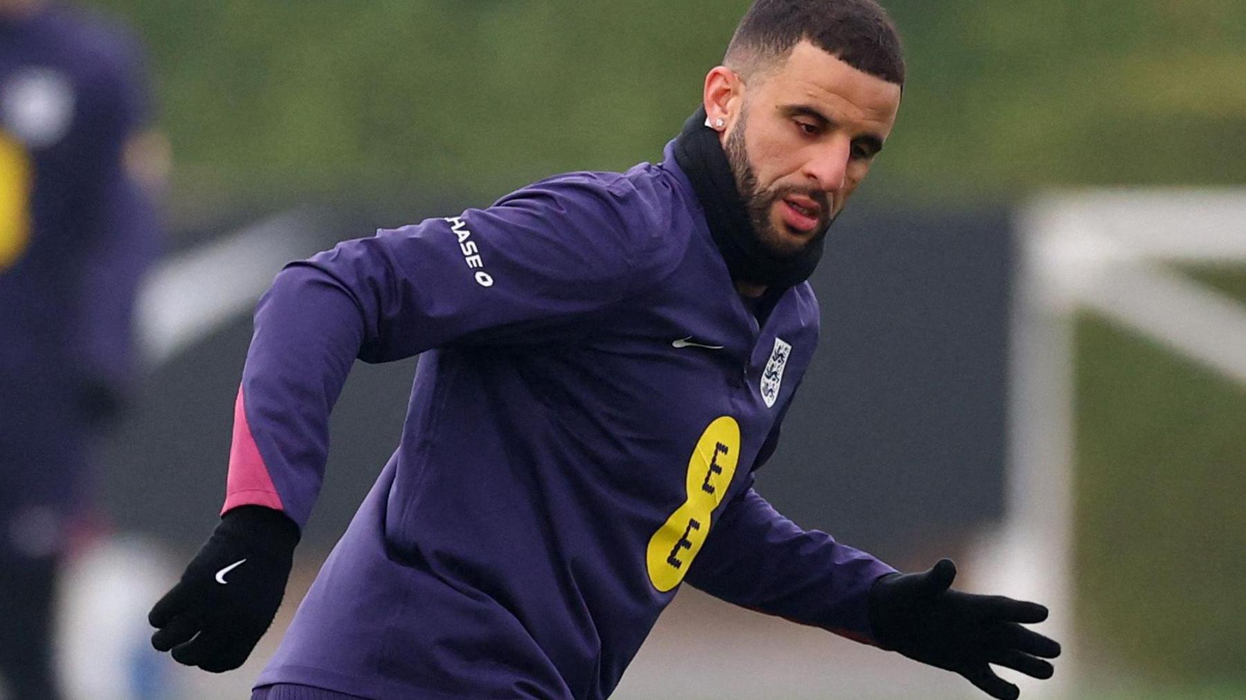 Kyle Walker training with the England squad. He is wearing a purple training top sporting the Three Lions badge, and a pair of black gloves.