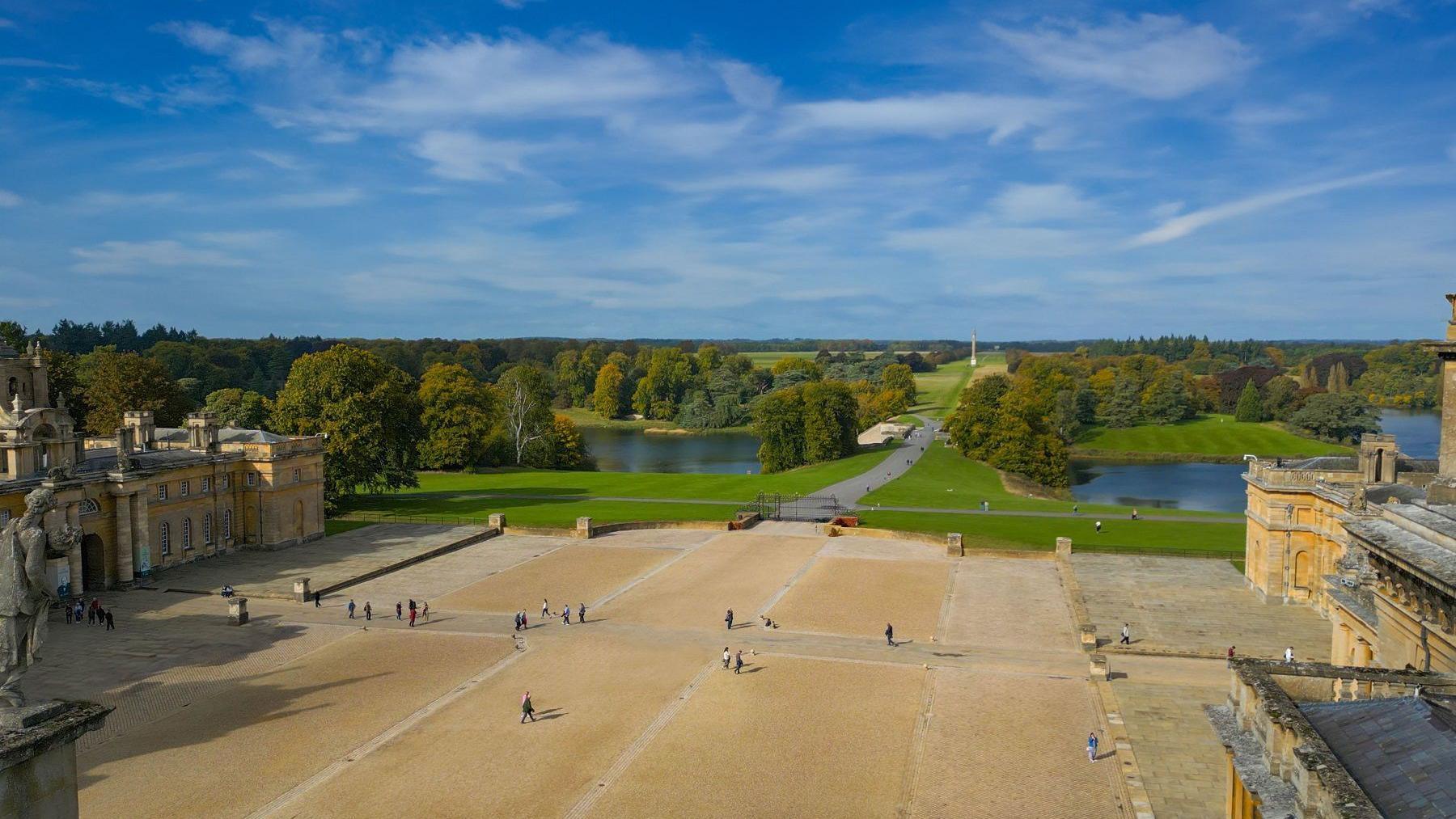 A panoramic view of the Blenheim Palace estate with visitors walking on the grounds. It's sunny.