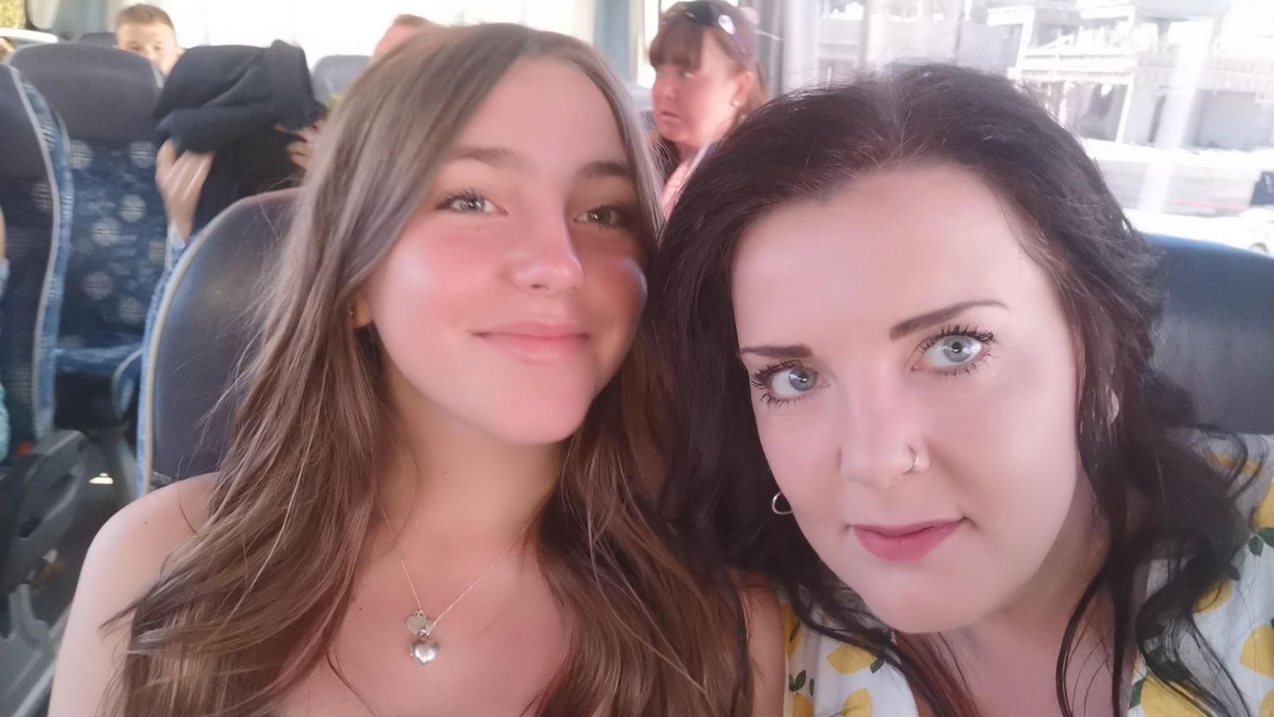 Chloe and her mother sitting together in a train carriage, faces next to each other and smiling