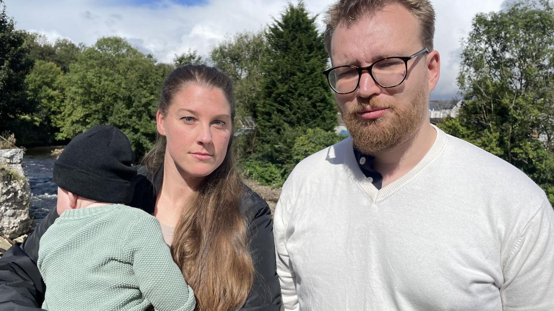 Justin and Imogen Crewe standing on the riverbank holding their small son 