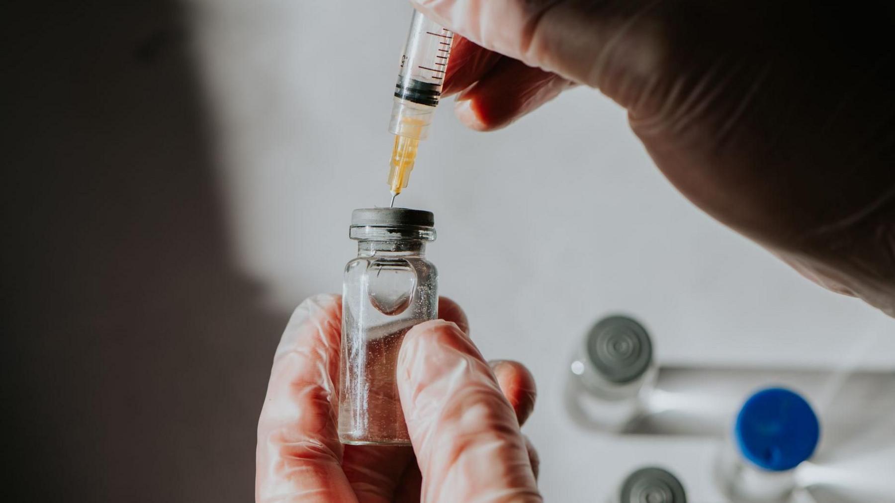 A scientist draws liquid medicine through a syringe from a vial