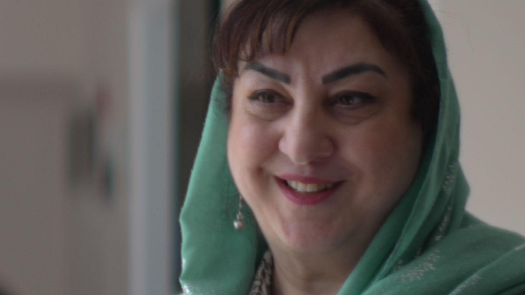 A Sikh lady with brown hair, wearing earrings and a green head covering.