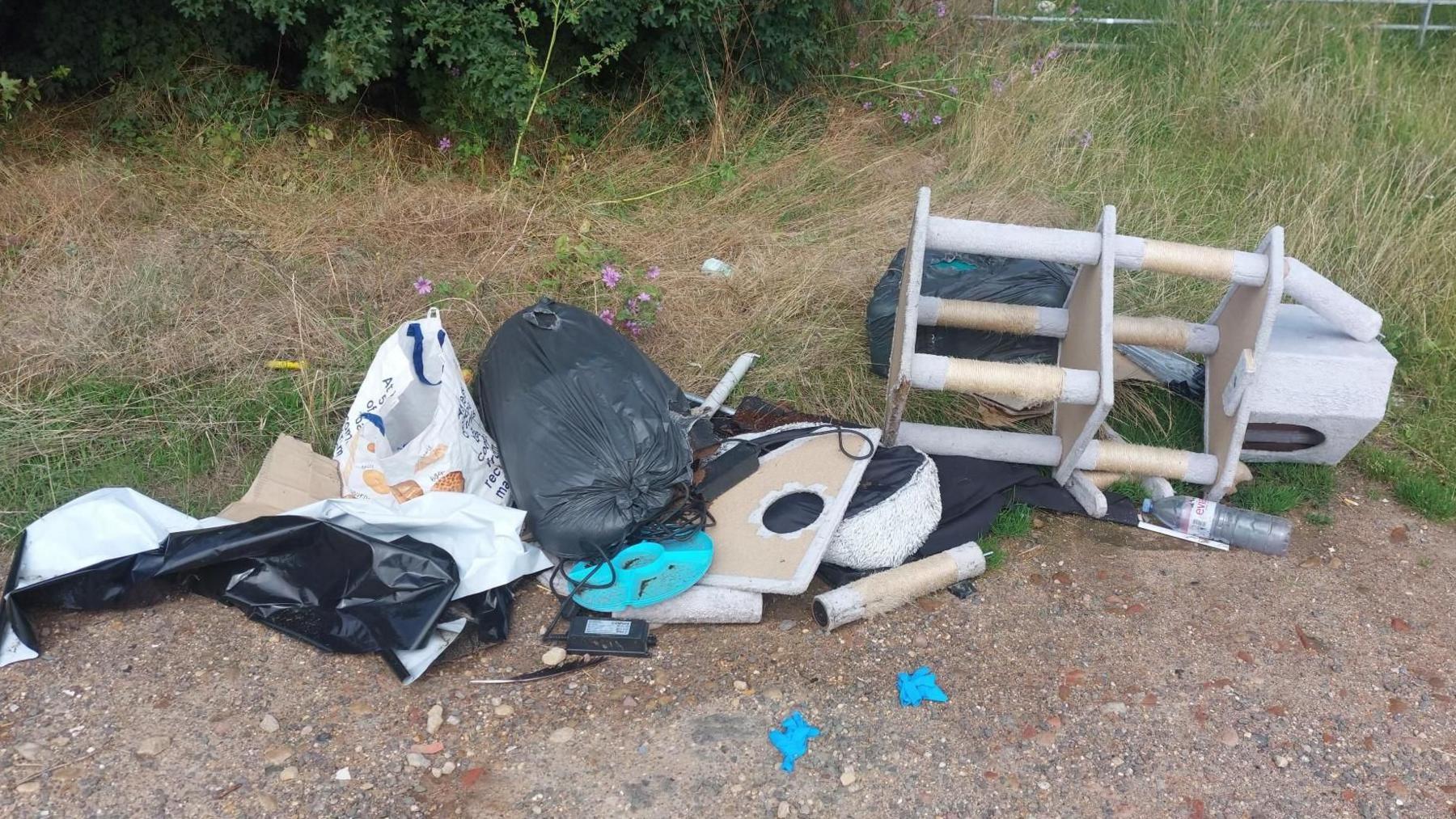 A close-up of fly-tipped rubbish. It shows bags of rubbish and broken household items dumped on grass.