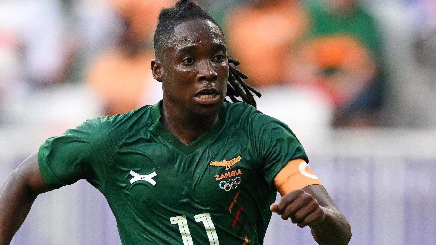 Barbra Banda in action for Zambia wears a green football shirt with an orange captain's armband with a white C on it