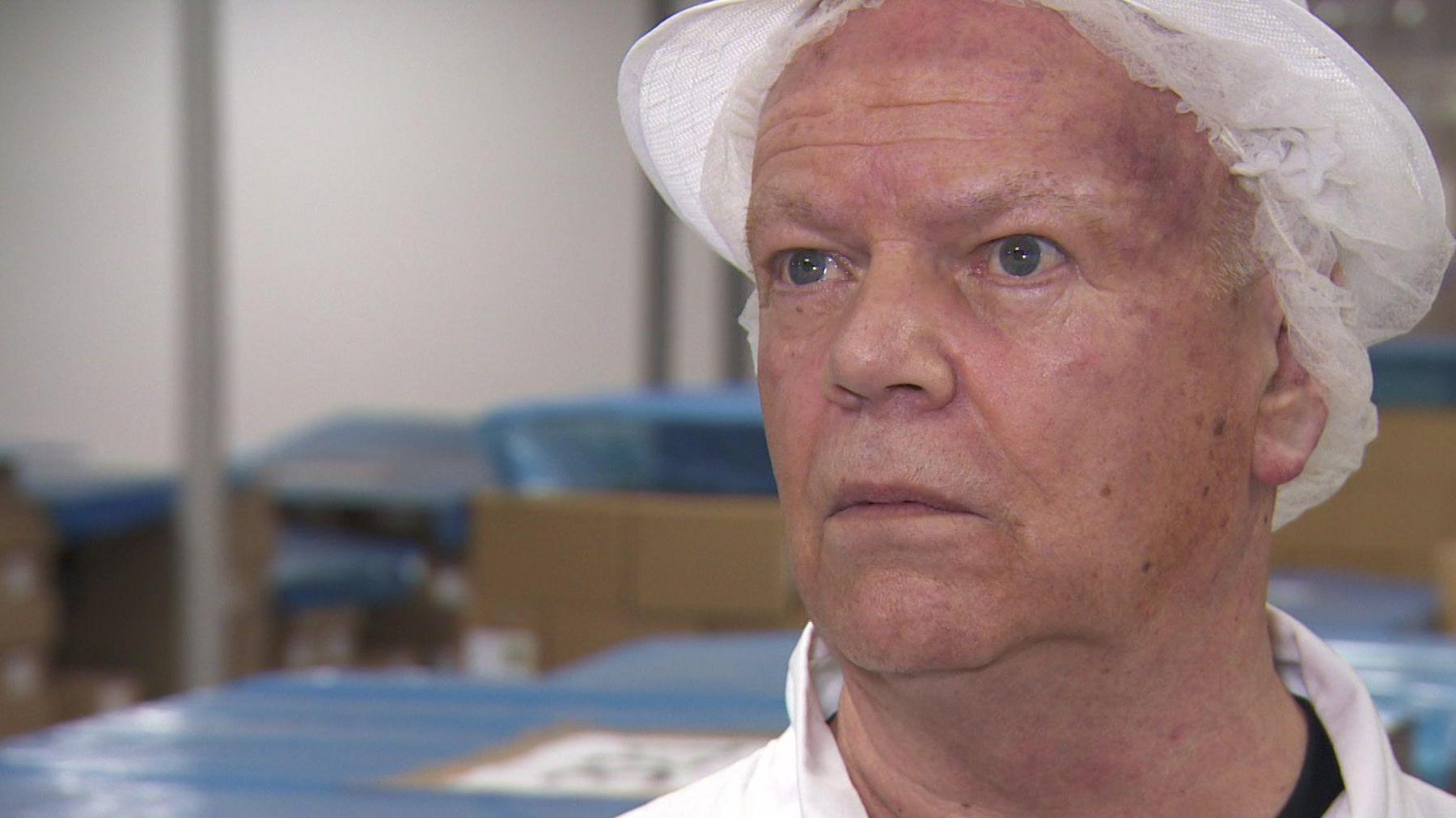 Beech's Fine Chocolates chairman Andrew Whiting wearing a white apron and white catering hair net in the chocolate factory.