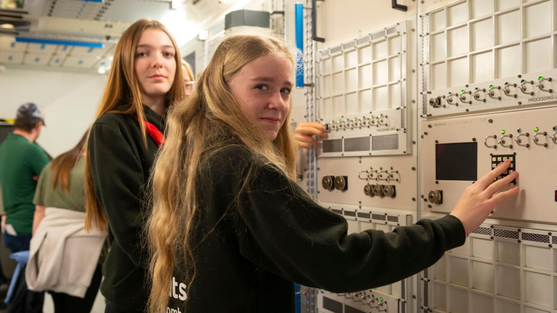 Two girls looking at camera with their hands on a number panel on the wall