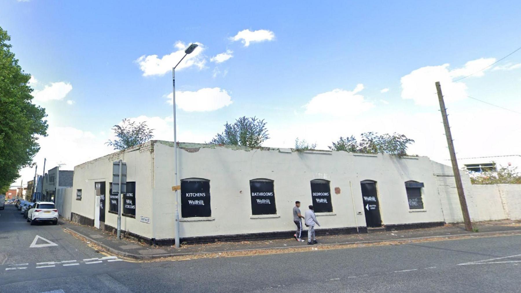 Nadeem House in Drayton Street, Wolverhampton, an industrial unit with white walls, a dilapidated roof and signs in its windows for the busines inside.