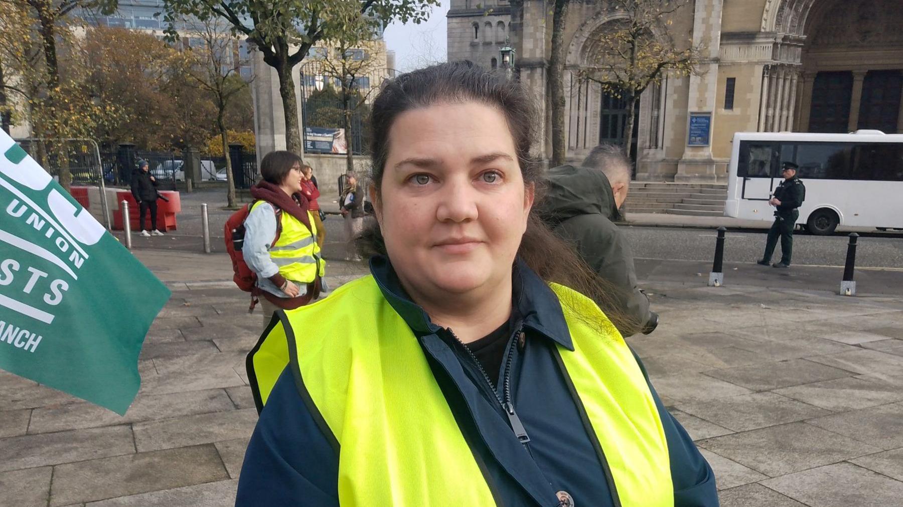 Ivanka Antova - a woman wearing a navy coat with a yellow hi-vis vest over the top. She has her dark hair tied back and is standing on the street looking at the camera.