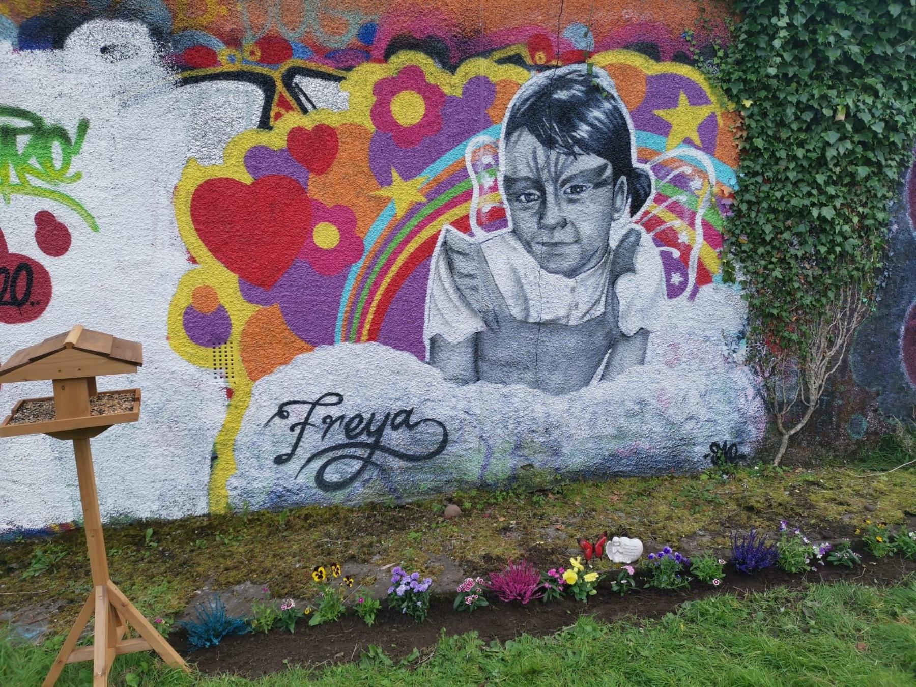 A painted wall memorial showing a young girl in black and white, with a brightly coloured background