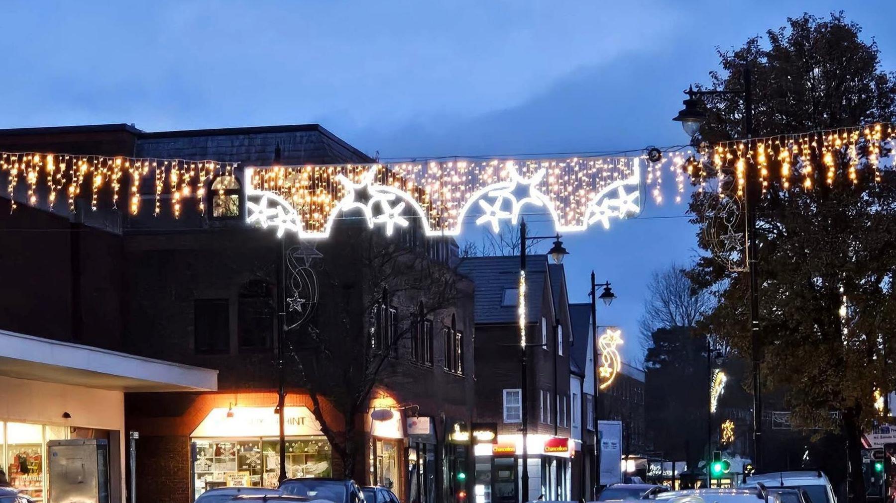 Christmas lights hanging across a busy street scene at twilight. The three of the lights are shaped like underwear, with stars and icicles also hanging down.