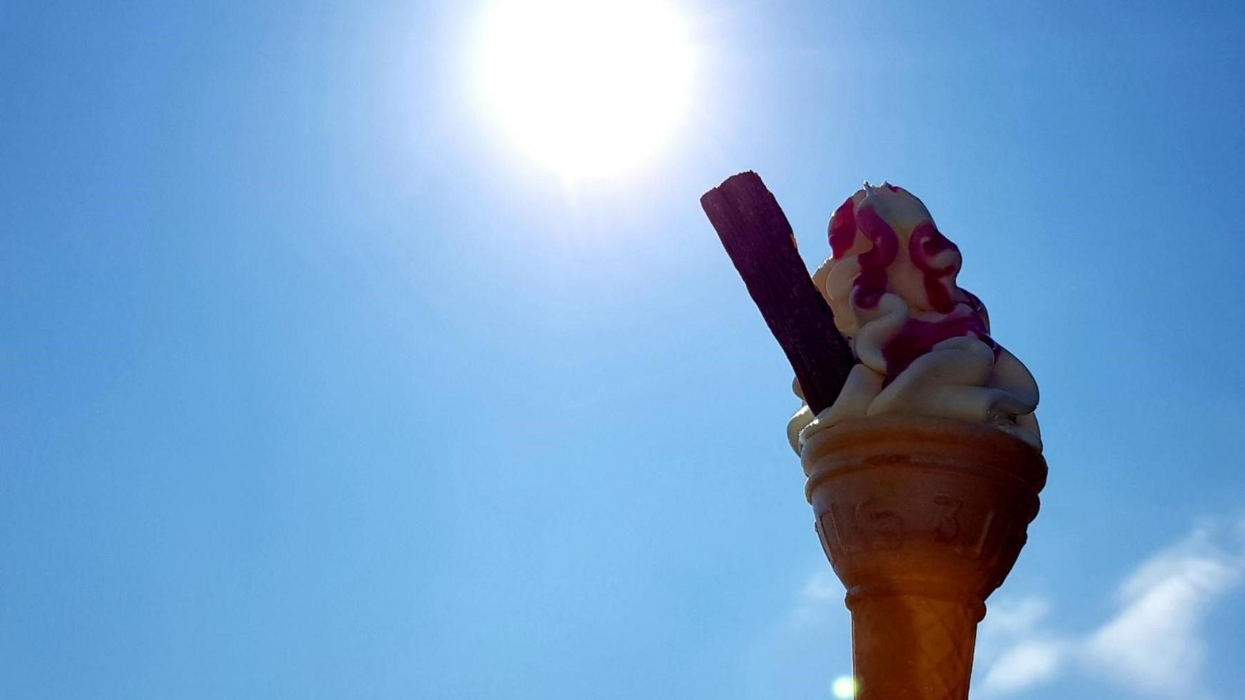 A 99 ice cream held up towards a bright Sun in a blue sky