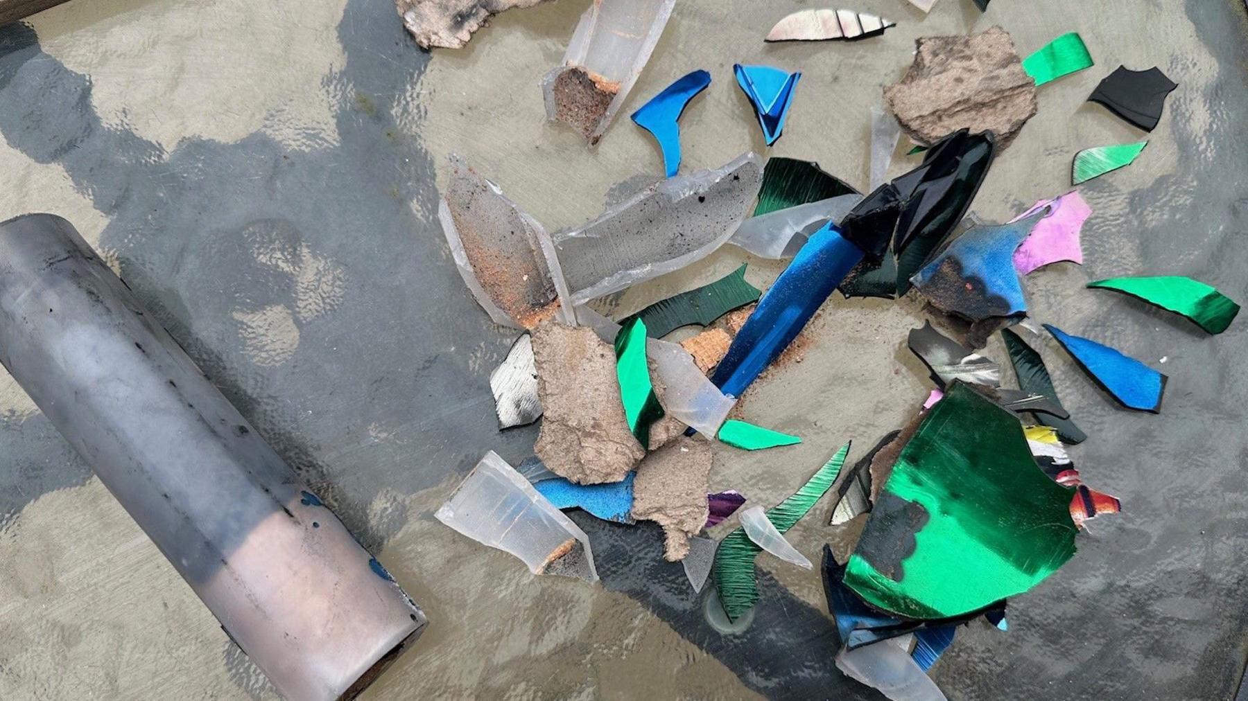 Remains of fireworks, including a plastic tube and pieces of brightly coloured, sharp-edged plastic, displayed on a garden table. The colours include blue, pink and green.