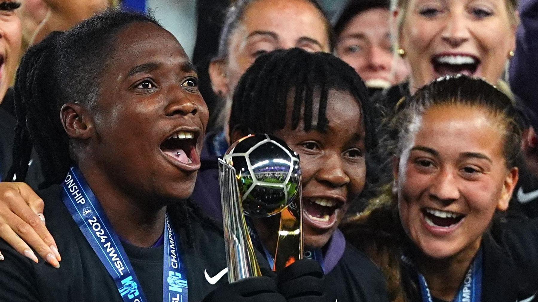 Barbra Banda holds the NWSL trophy in gloved hands as team-mates gather around her to celebrate Orlando Pride winning the NWSL Championship final