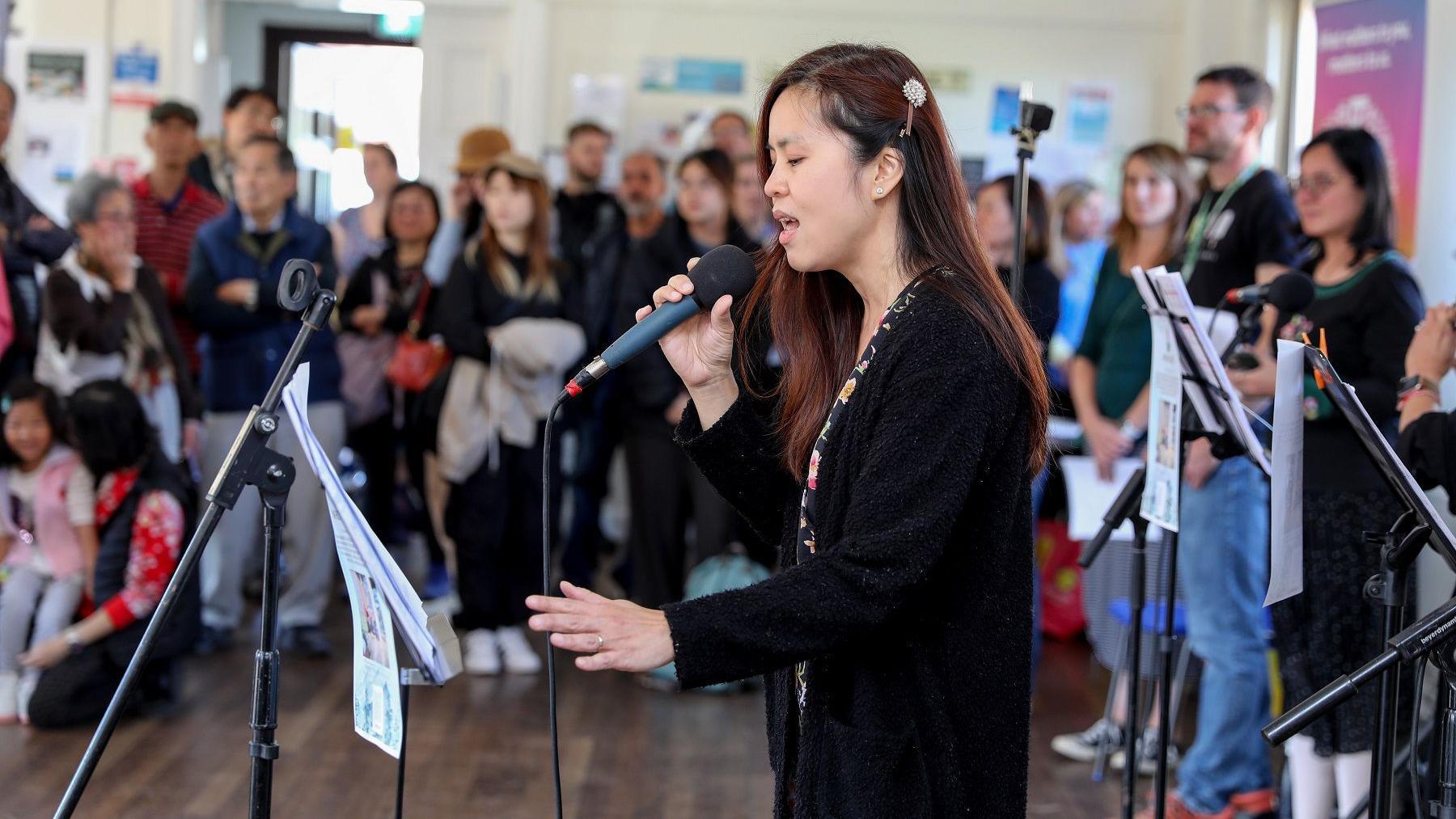 A woman from the South Gloucestershire Hong Kong community sings into a microphone while dozens of people watch on during the Mid Autumn Festival celebrations in Yate Parish Hall