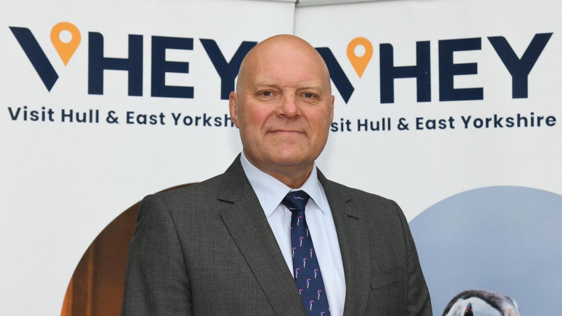 Portrait of Chris Blacksell, VHEY's chairman. He is wearing a grey patterned suit, white shirt and dark navy tie