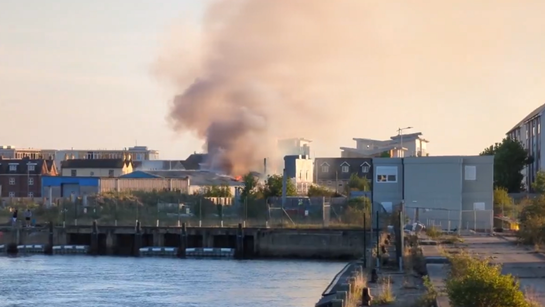 A building fire in the distance, with a glimpse of orange flame, as viewed from the quay.