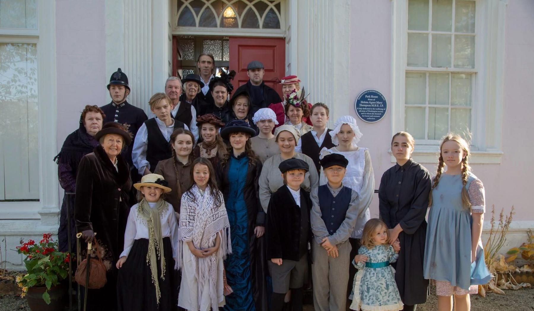 A large group of actors in Victorian clothing stands on the steps of the Helena Thompson museum in Workington.